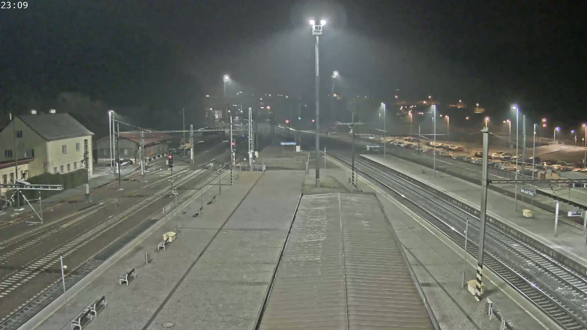 A nighttime view of a train station with several tracks, platforms, and a parking lot under foggy conditions.