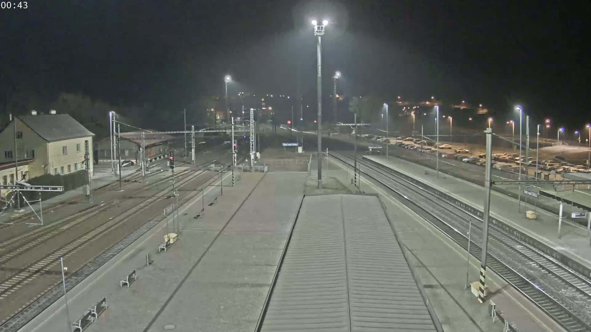 A nighttime view of a train station with several tracks, platforms, and a parking lot, illuminated by numerous lights.