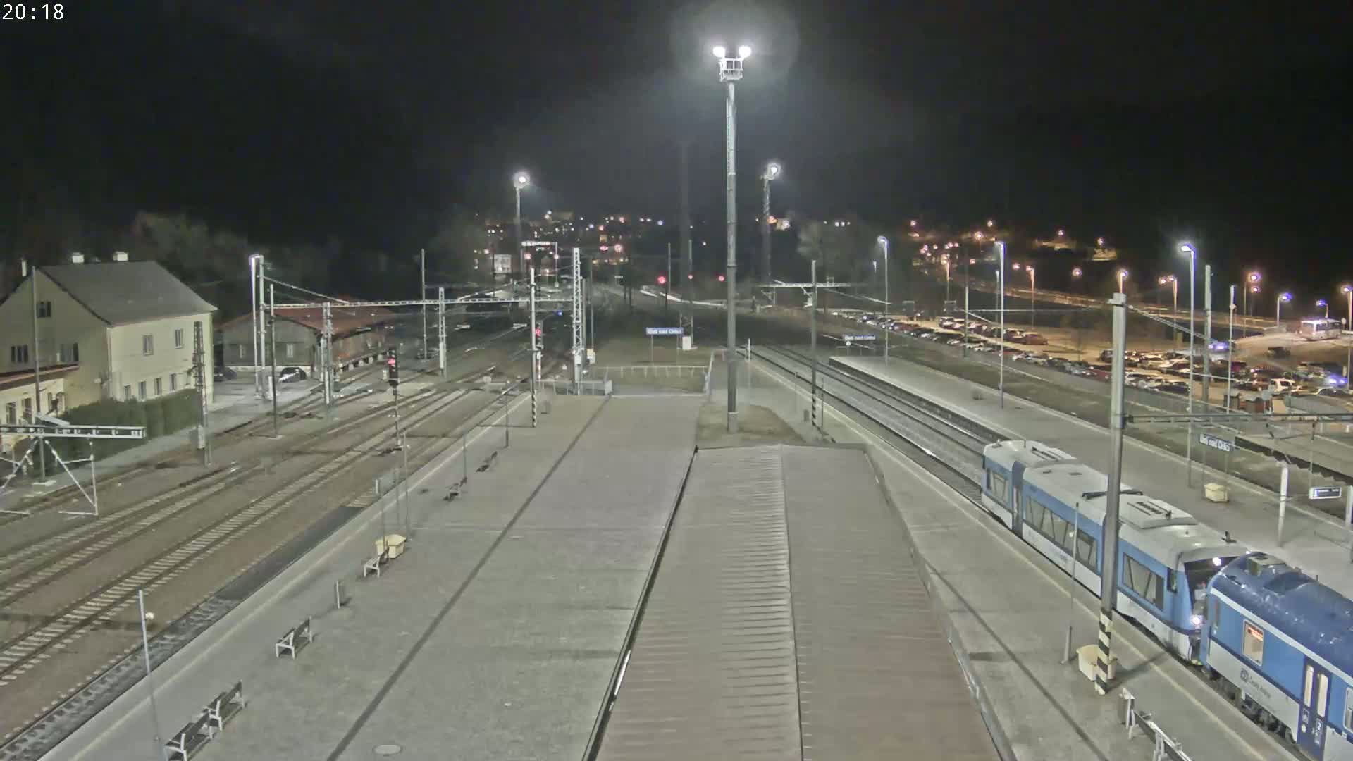 A nighttime view of a train station with a train arriving at a platform under clear skies.