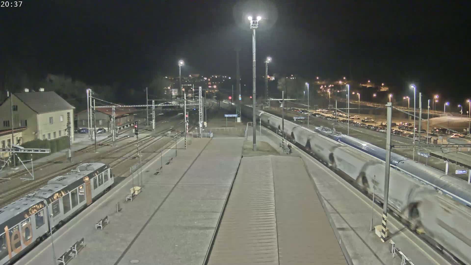 A nighttime view of a train station with a train departing and another train arriving, under clear skies.