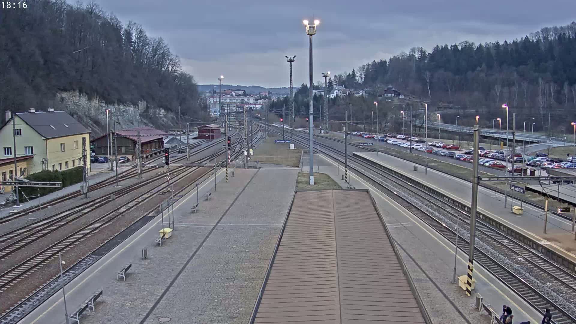 A train station with multiple tracks and a parking lot, situated on a hill under an overcast sky.