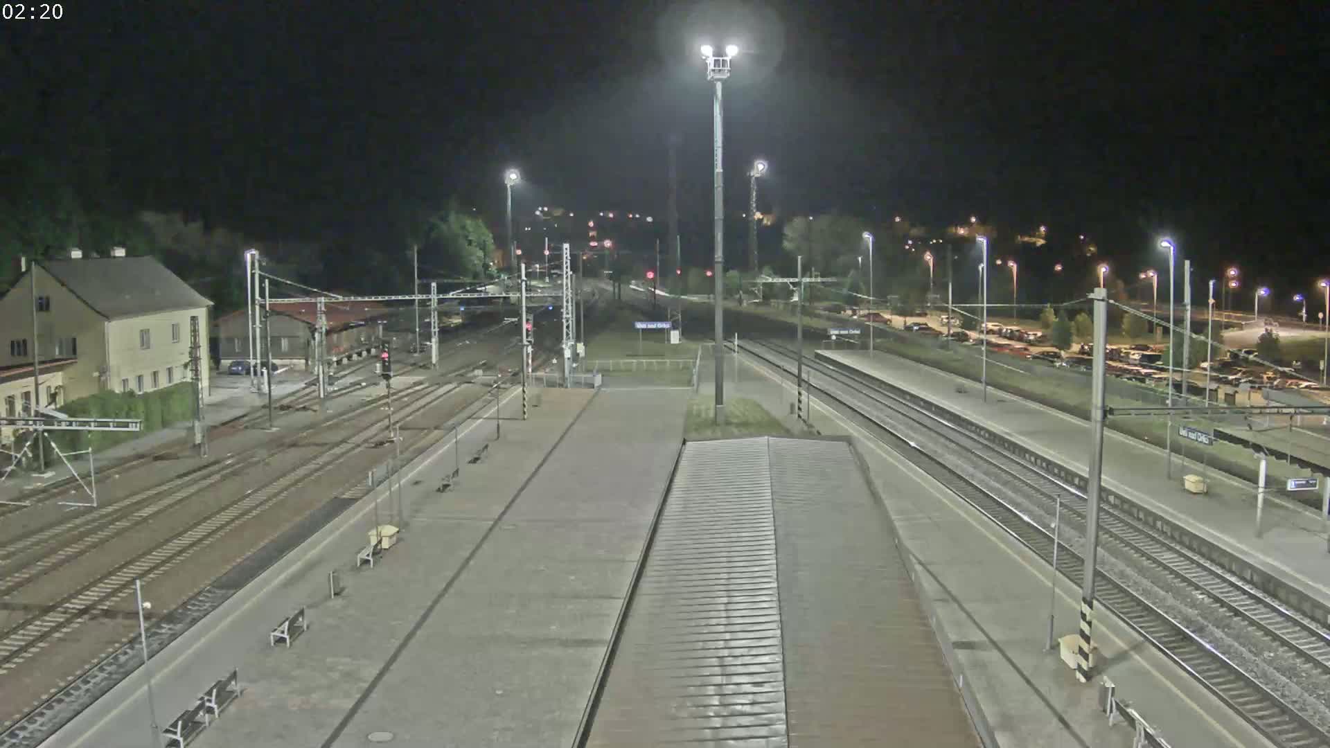 A nighttime view of a train station with multiple train tracks, a building, and a parking lot.