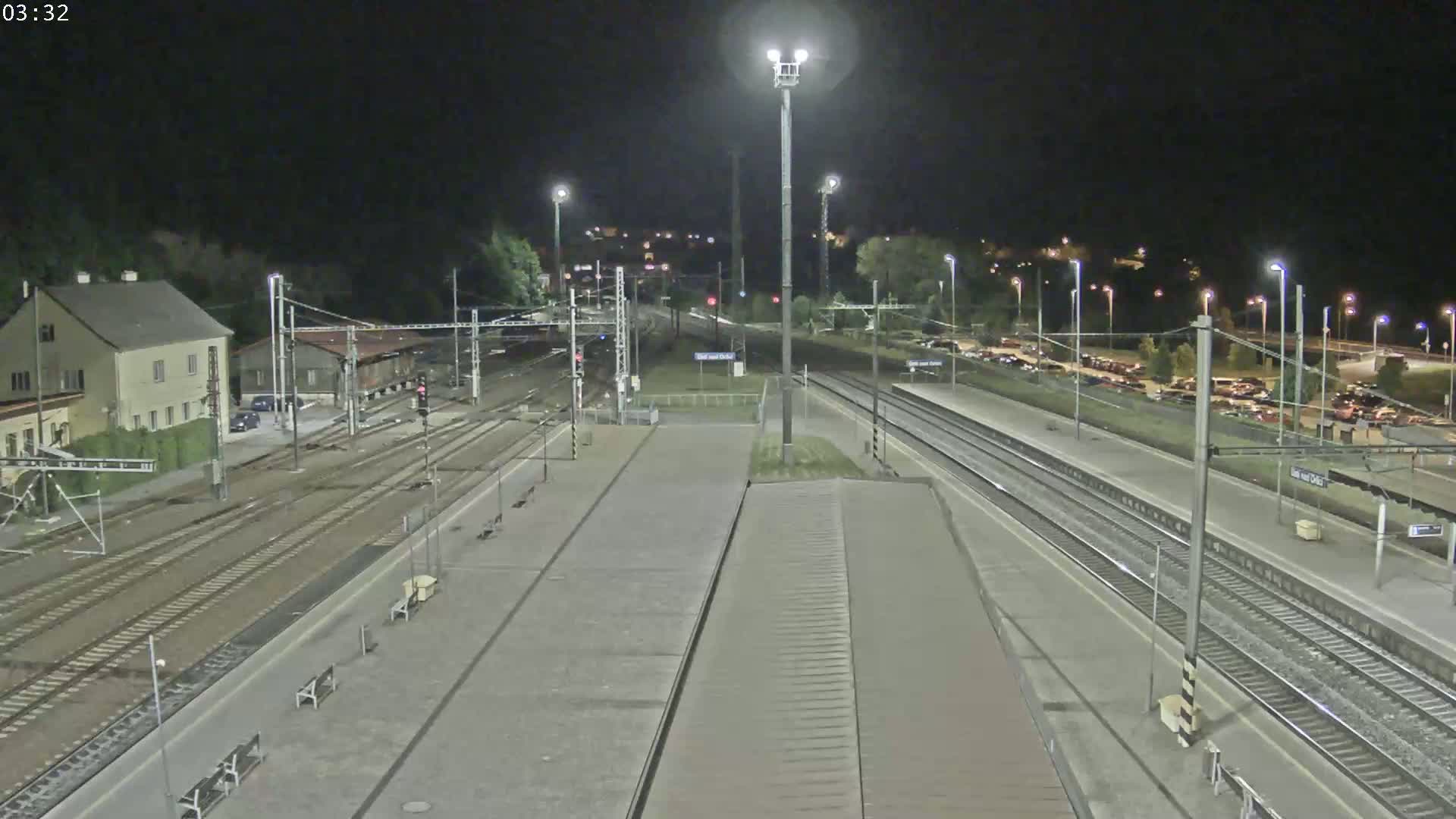 A nighttime view of a train station with multiple tracks, platforms, and a parking lot, illuminated by streetlights.