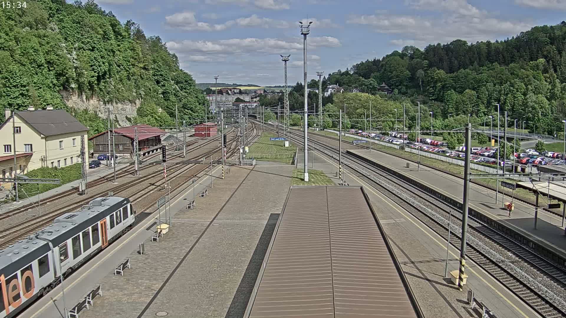 A train sits at a station platform next to several railway tracks under a partly sunny sky.