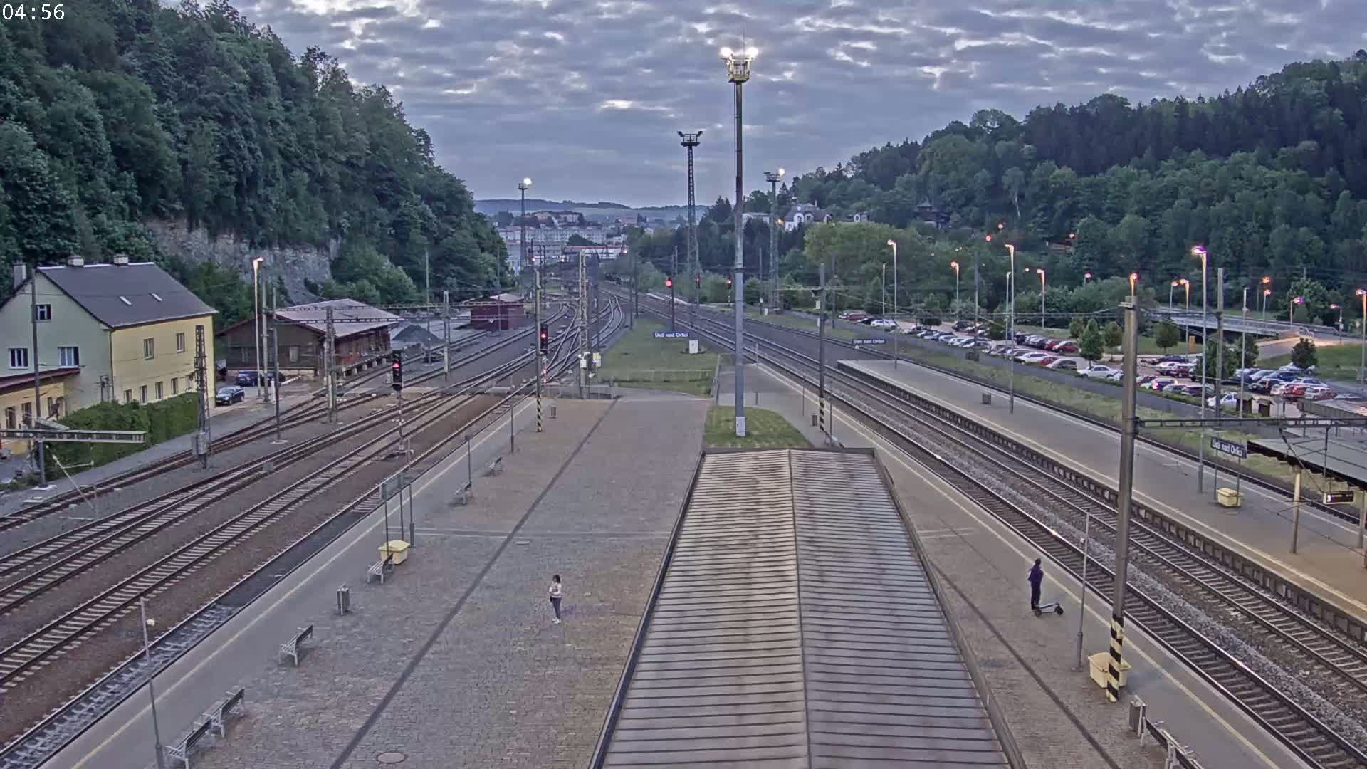 A train station with numerous tracks, surrounded by buildings and greenery under an overcast sky.