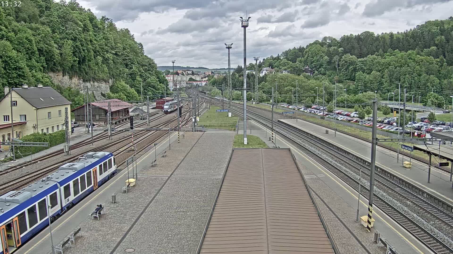 A train station with multiple tracks, a partly cloudy sky, and a train at a platform.