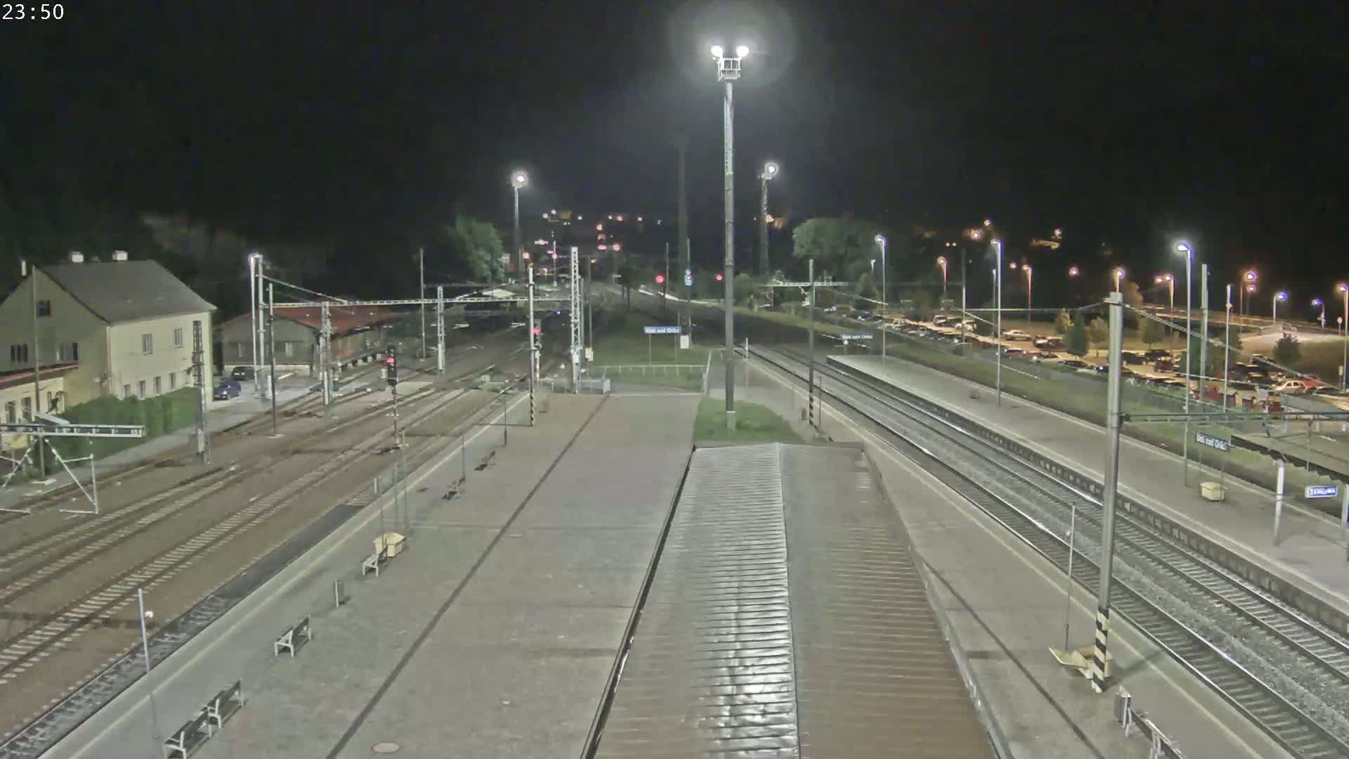 A nighttime view of a train station with multiple tracks, platforms, and a parking lot, under clear skies.