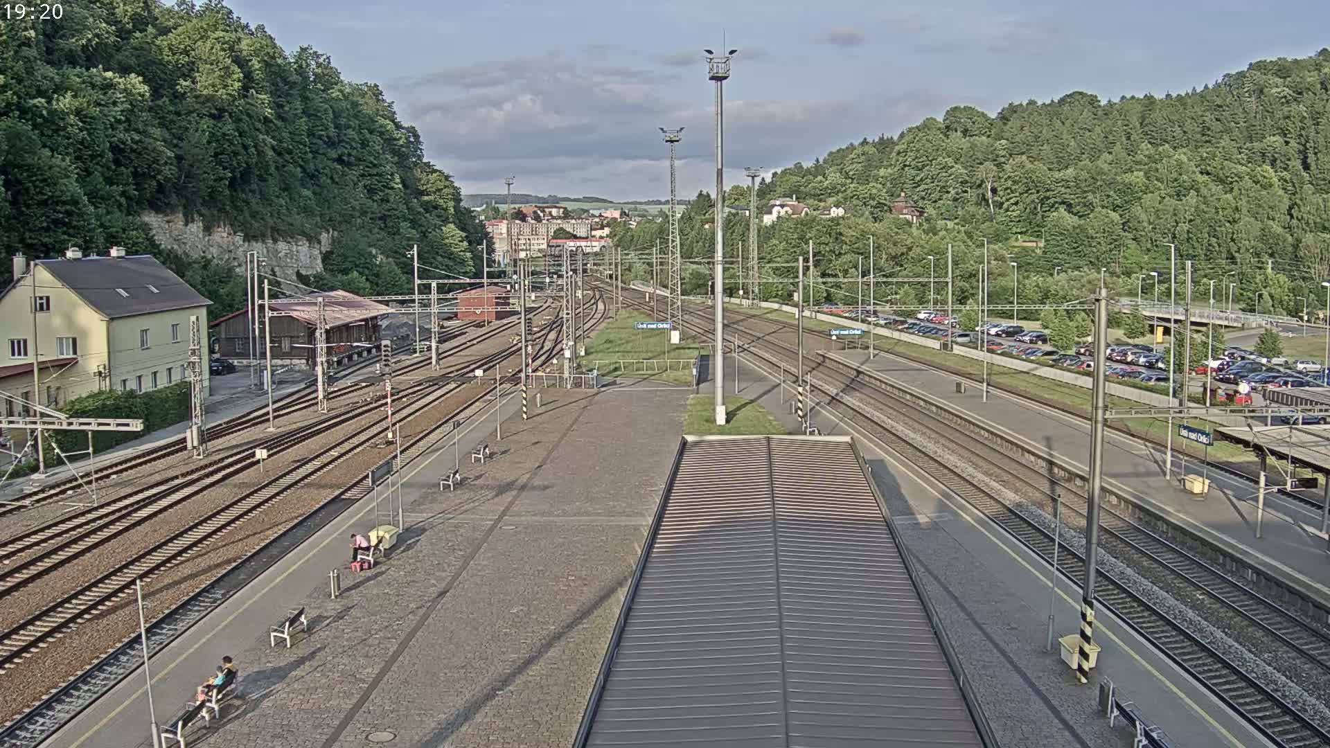 A high-angle view of a train station with numerous tracks, platforms, and a parking lot, under partly cloudy skies.