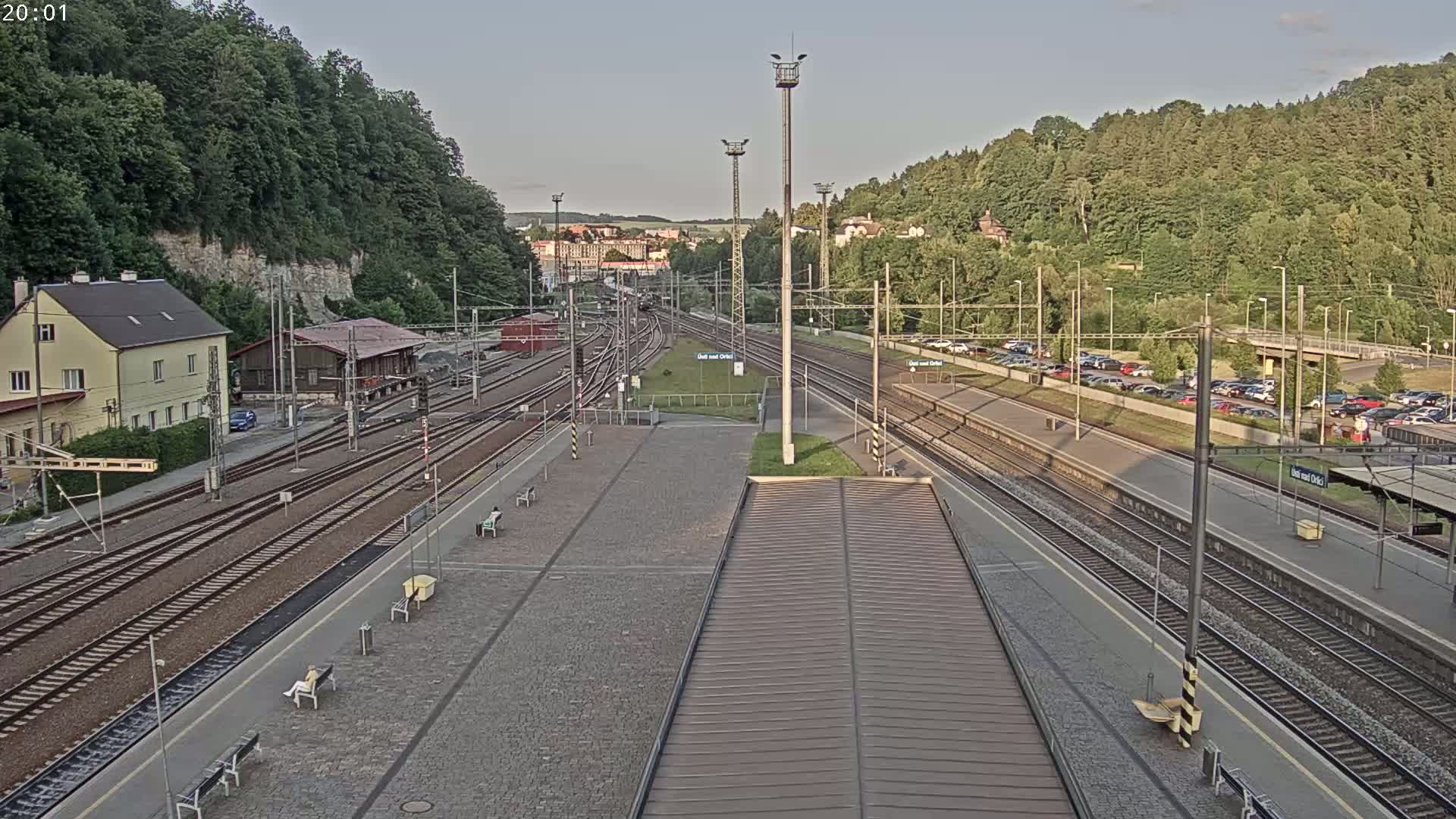 A train station with multiple tracks, platforms, and a parking lot is seen on a partly cloudy evening.