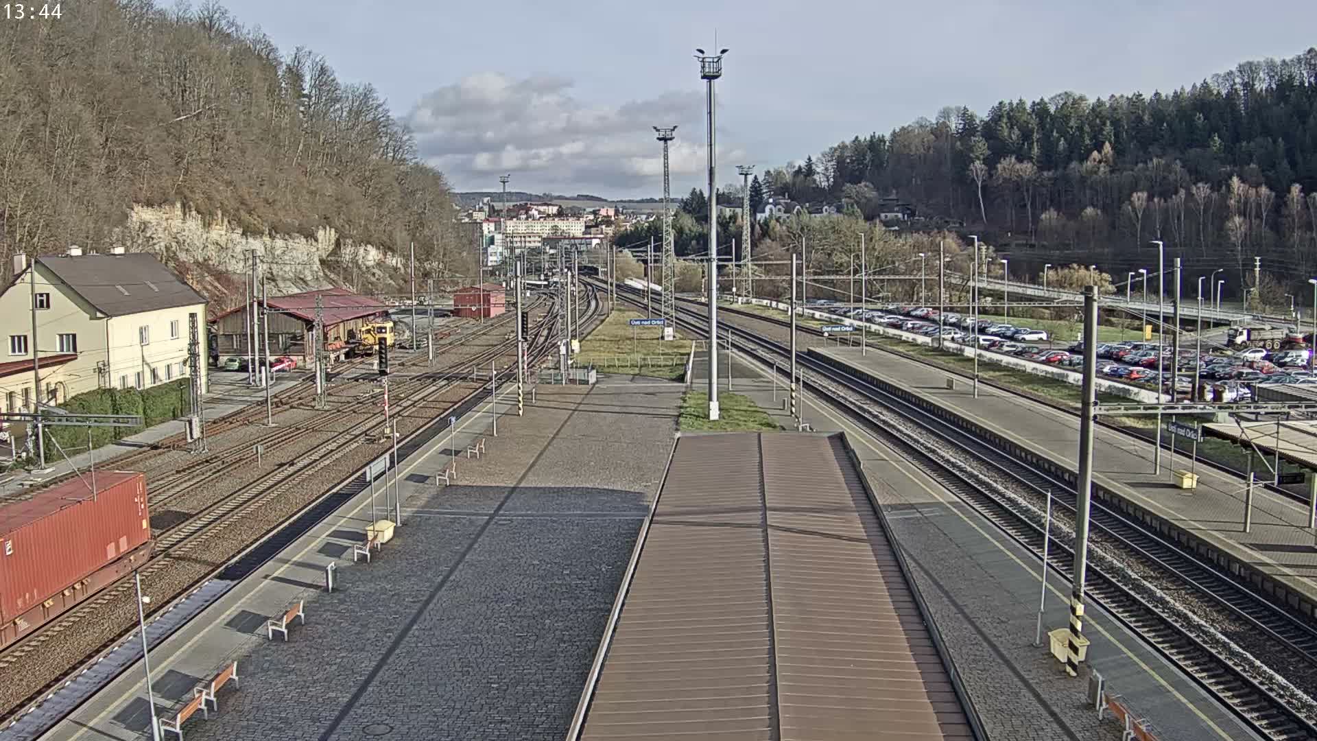 A nighttime view of a train station with a train at a platform, multiple tracks, and a parking lot visible in the background under dark skies.
