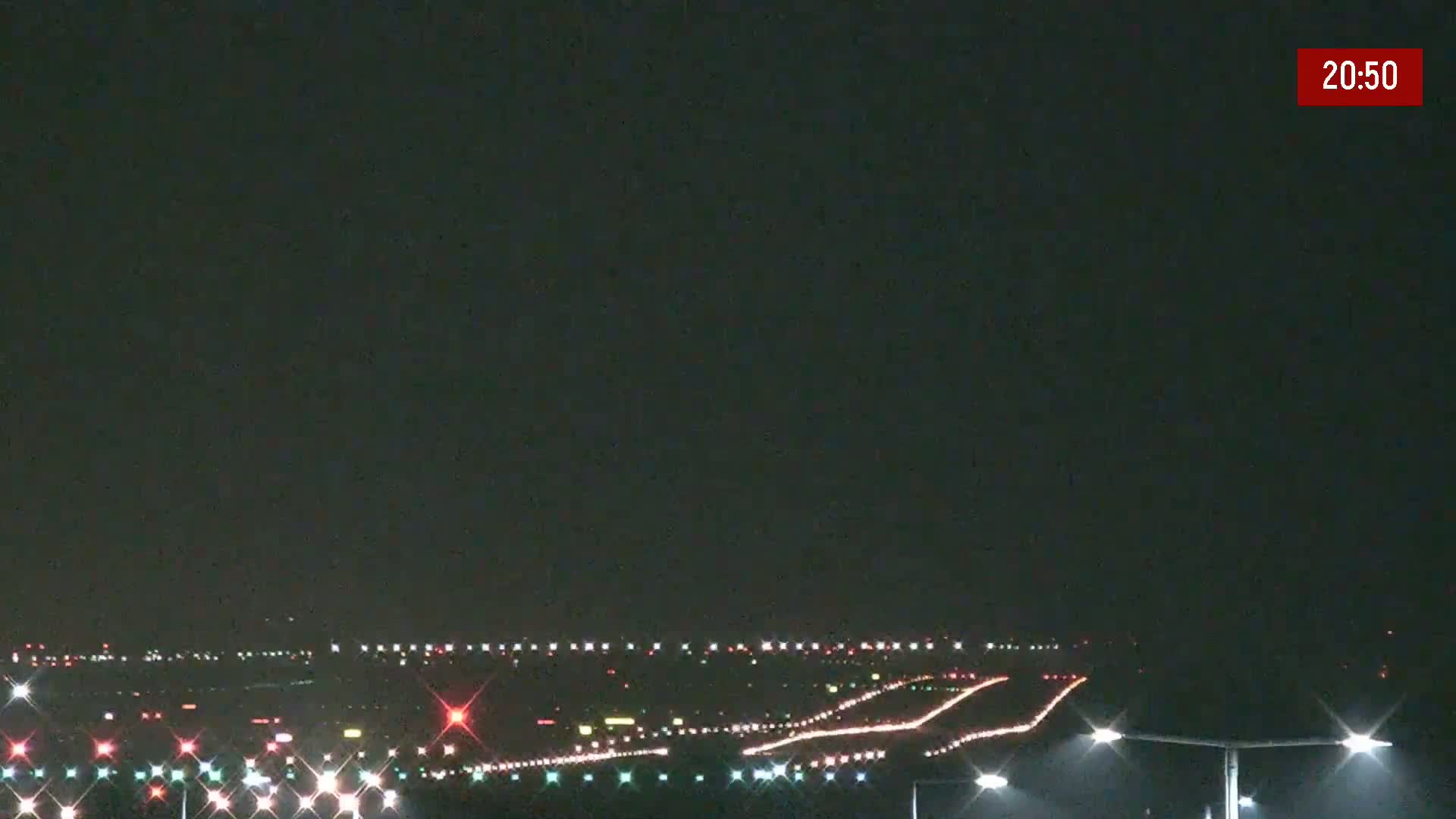 A nighttime view of an airport runway illuminated with lights under a dark, clear sky.