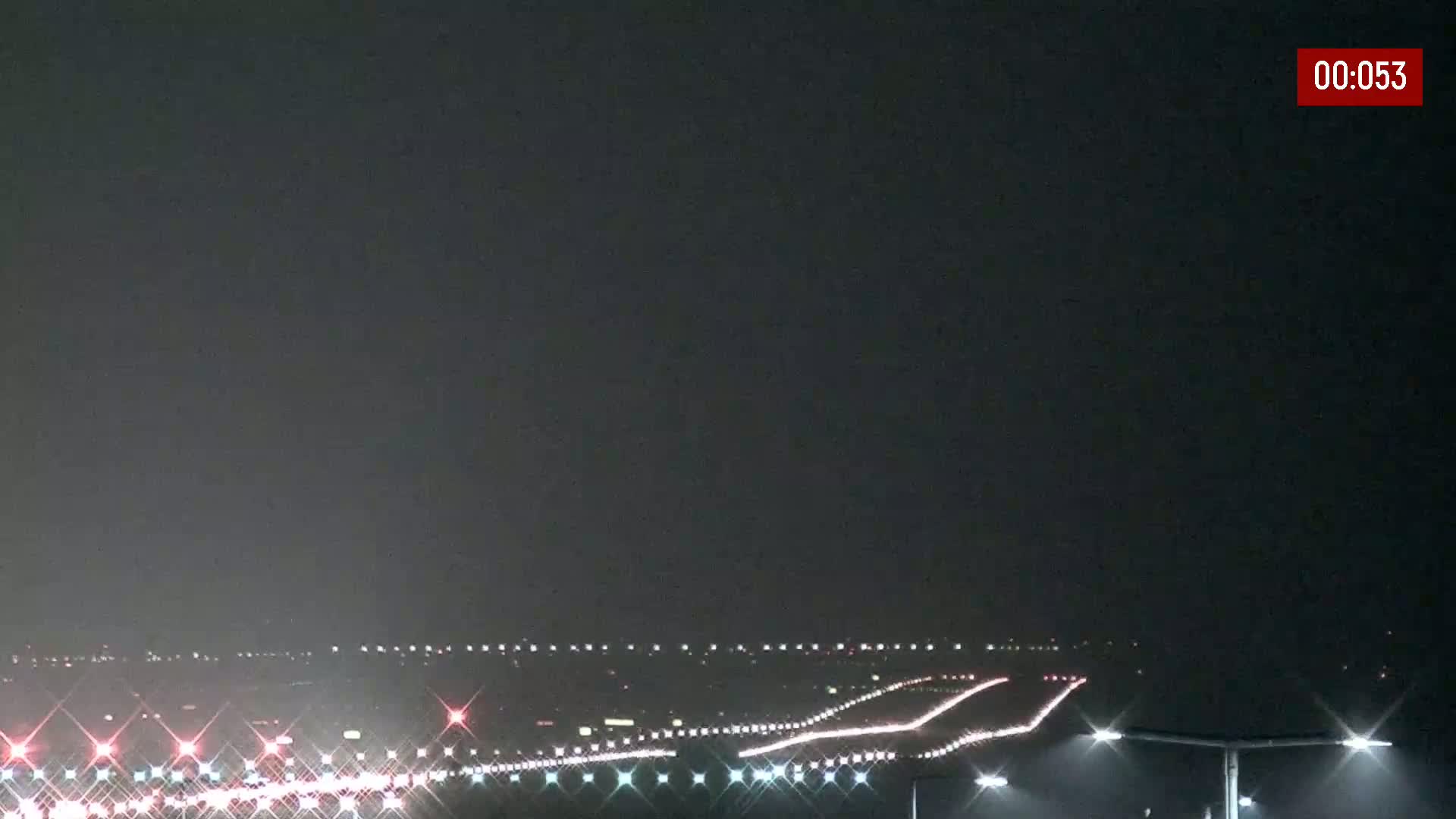 Under a dark, possibly overcast night sky, a long stretch of highway with many cars driving on it is illuminated by streetlights.