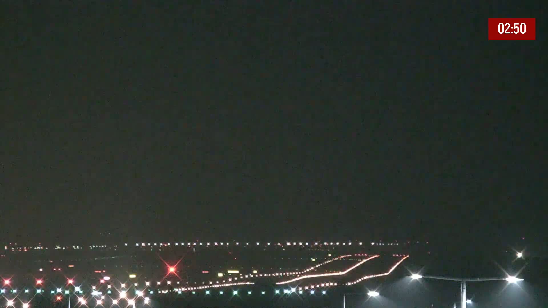 At night, under a dark sky, airport runway lights illuminate a mostly empty tarmac.