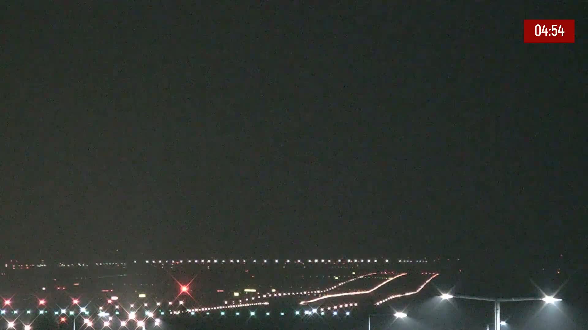 A nighttime view of an airport runway illuminated by lights under a dark, clear sky.
