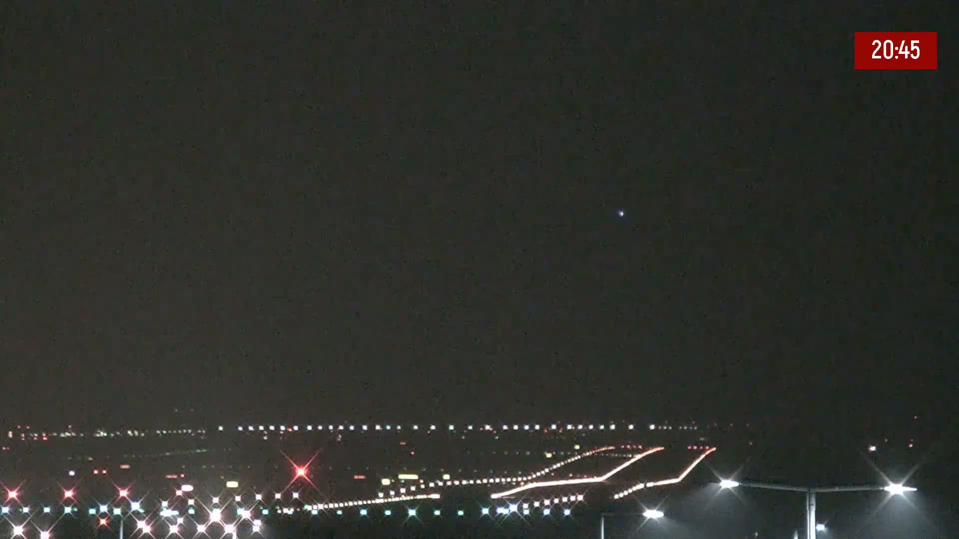 A nighttime long shot of an airport runway illuminated by lights under a dark, clear sky.