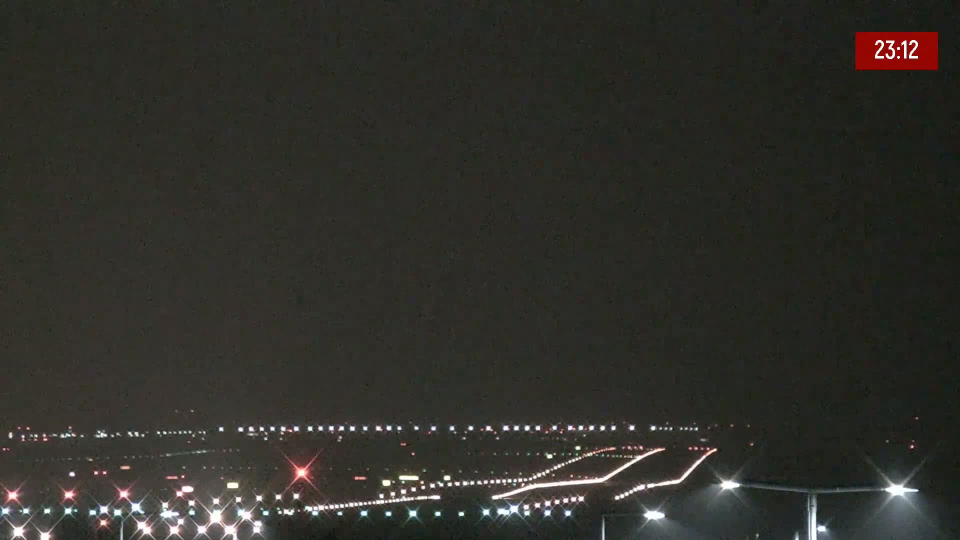 A nighttime long shot of an airport runway with its lights illuminated under a dark sky.