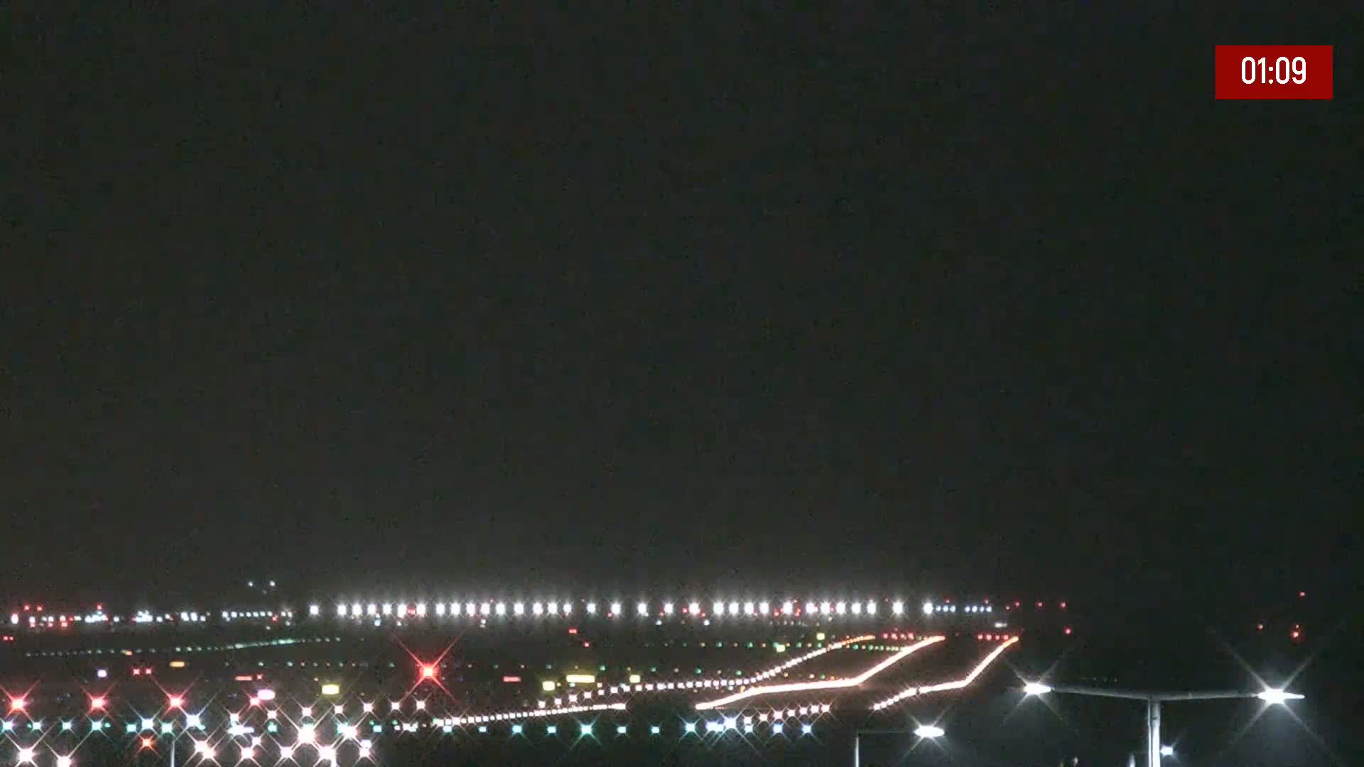 A nighttime long shot of an airport runway illuminated by bright lights under a dark sky.