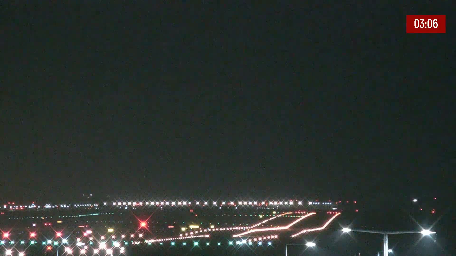 A nighttime view of an airport runway illuminated with lights under a dark, clear sky.