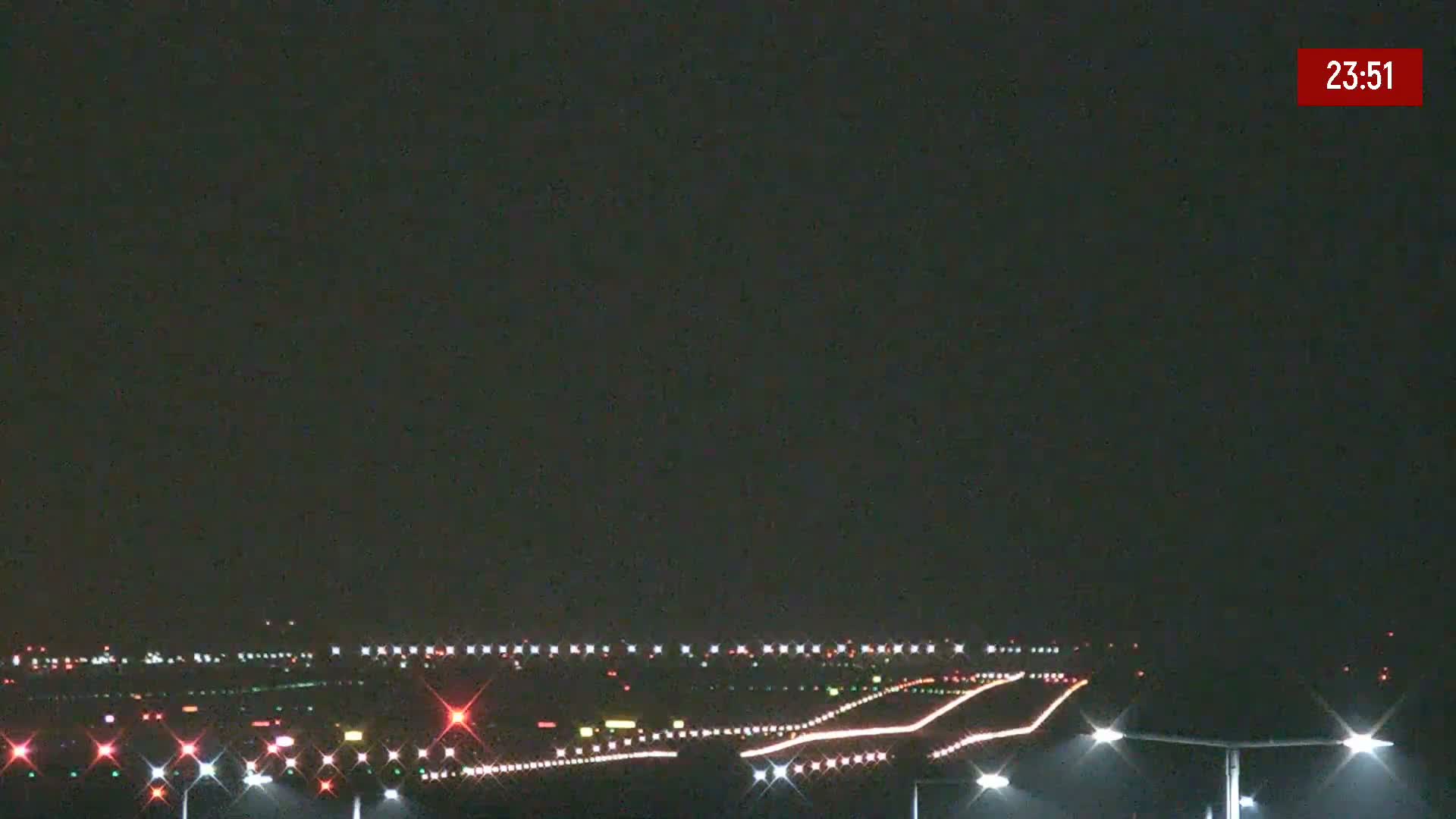 A nighttime long shot of an airport runway illuminated with lights under a dark sky.