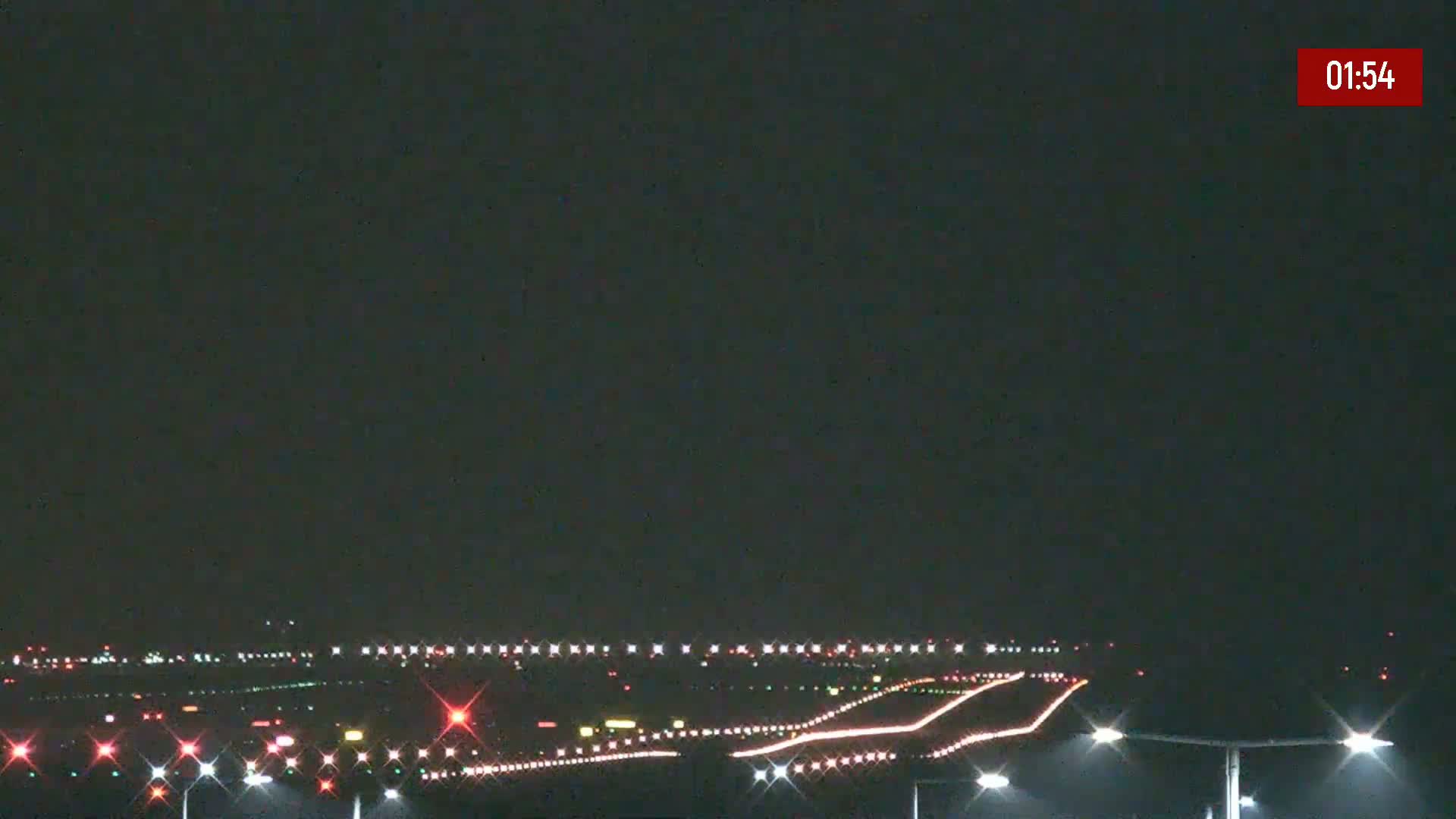 At night, runway lights illuminate a dark airport tarmac under a clear, dark sky.
