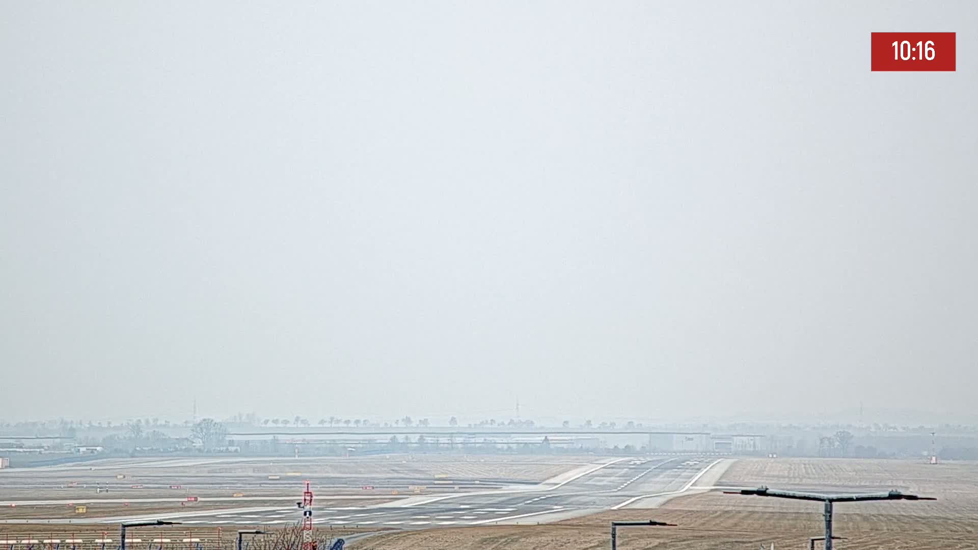 A hazy view of an airport runway and surrounding flat land under a light overcast sky.