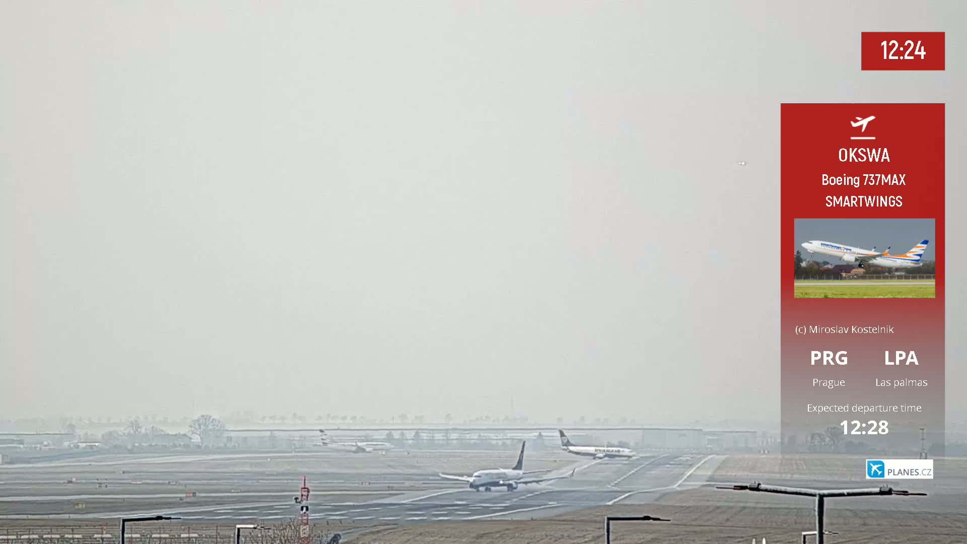 A hazy airport runway with several airplanes, one of which is taxiing toward takeoff.