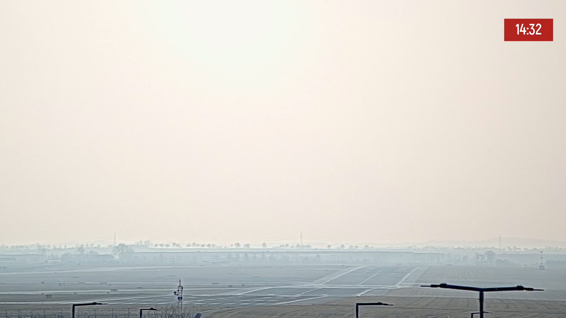 A hazy view of an airport runway and surrounding flat land under a bright, hazy sky.