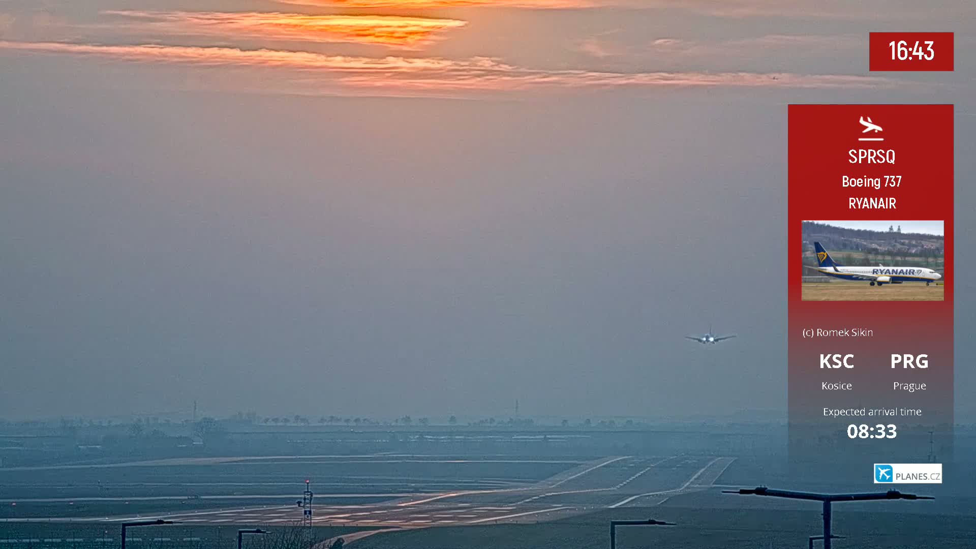 A hazy sunset illuminates an airport runway as a small airplane approaches during landing.