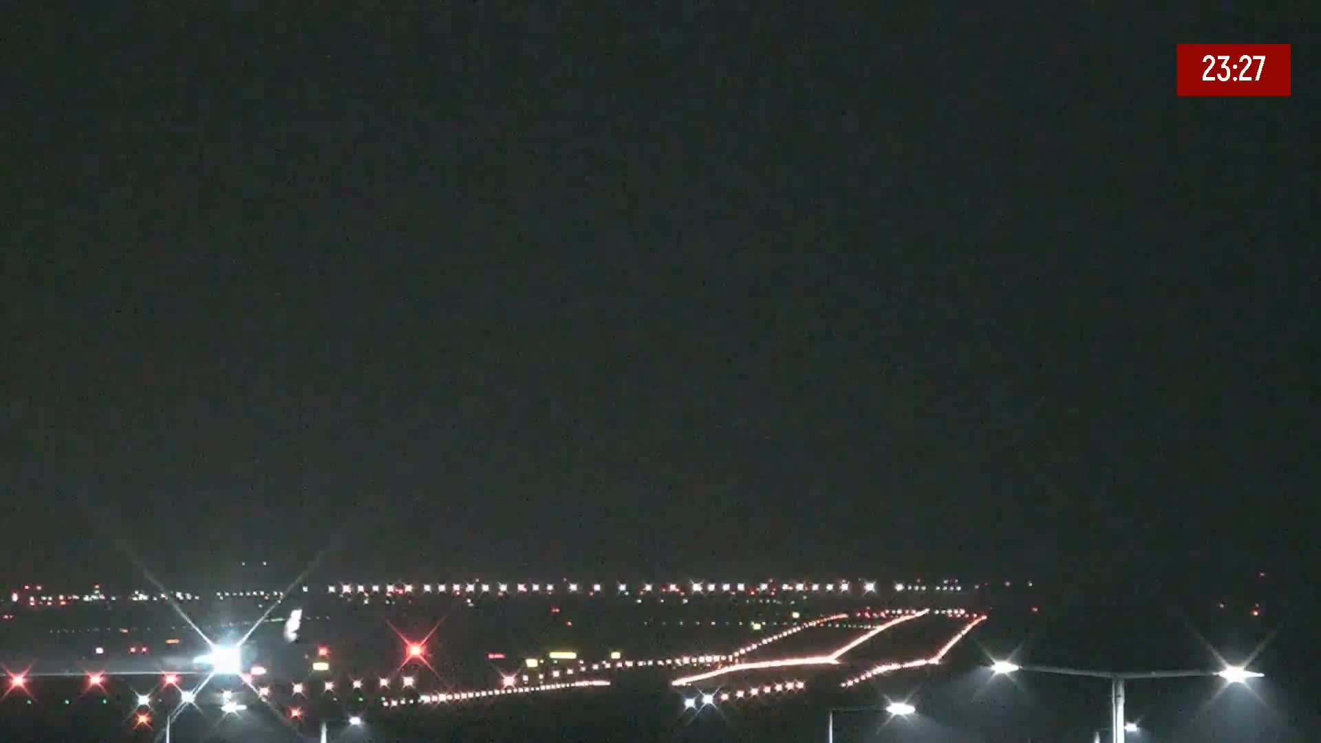 A nighttime view of an airport runway illuminated by lights under a clear, dark sky.