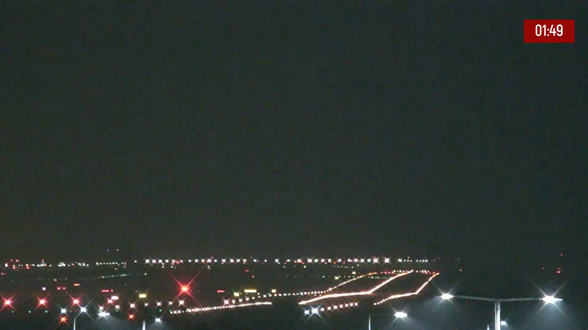 At night, under a dark sky, runway lights illuminate a long airport runway.
