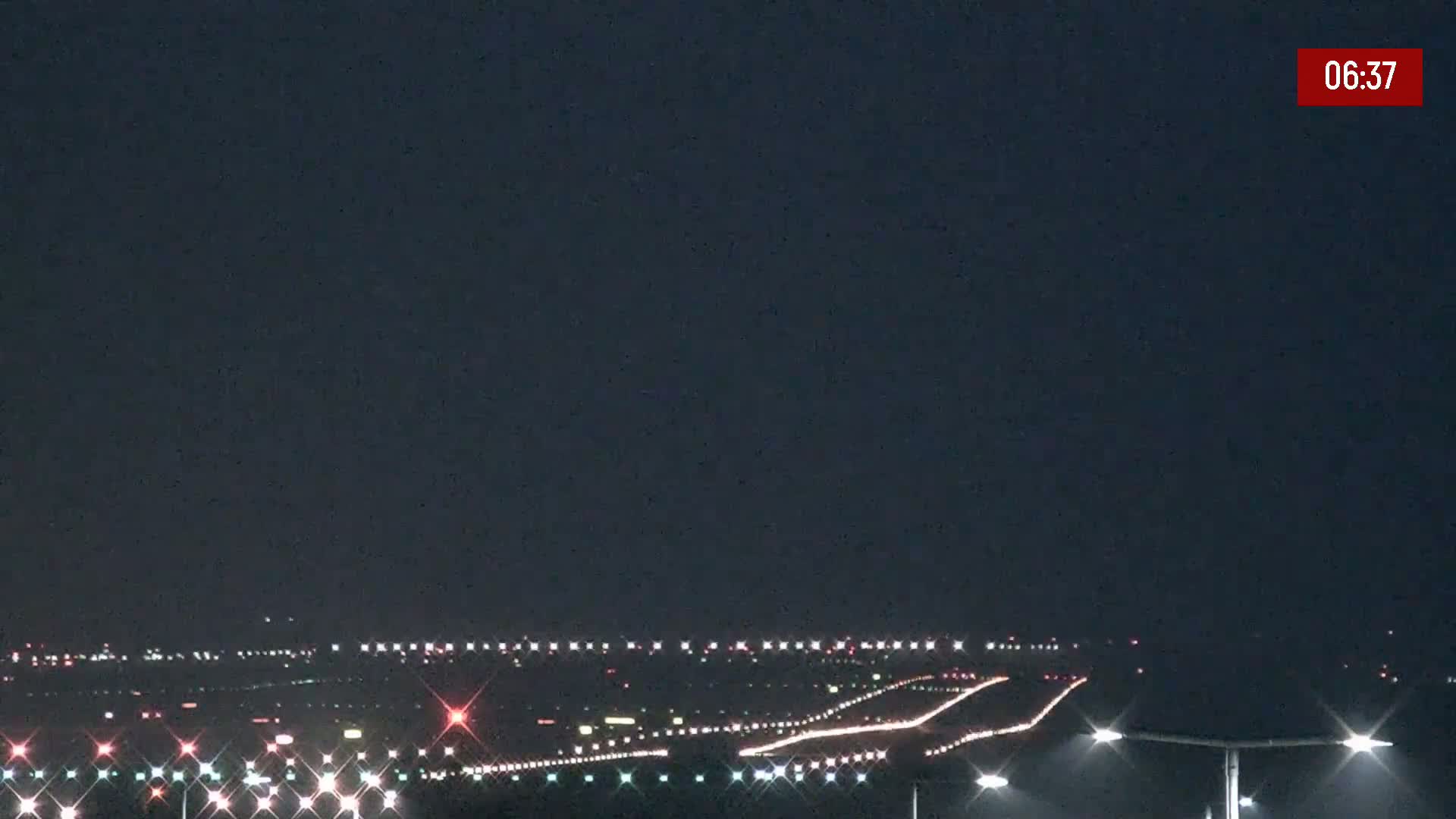 A nighttime view of an airport runway illuminated by lights under a dark sky.