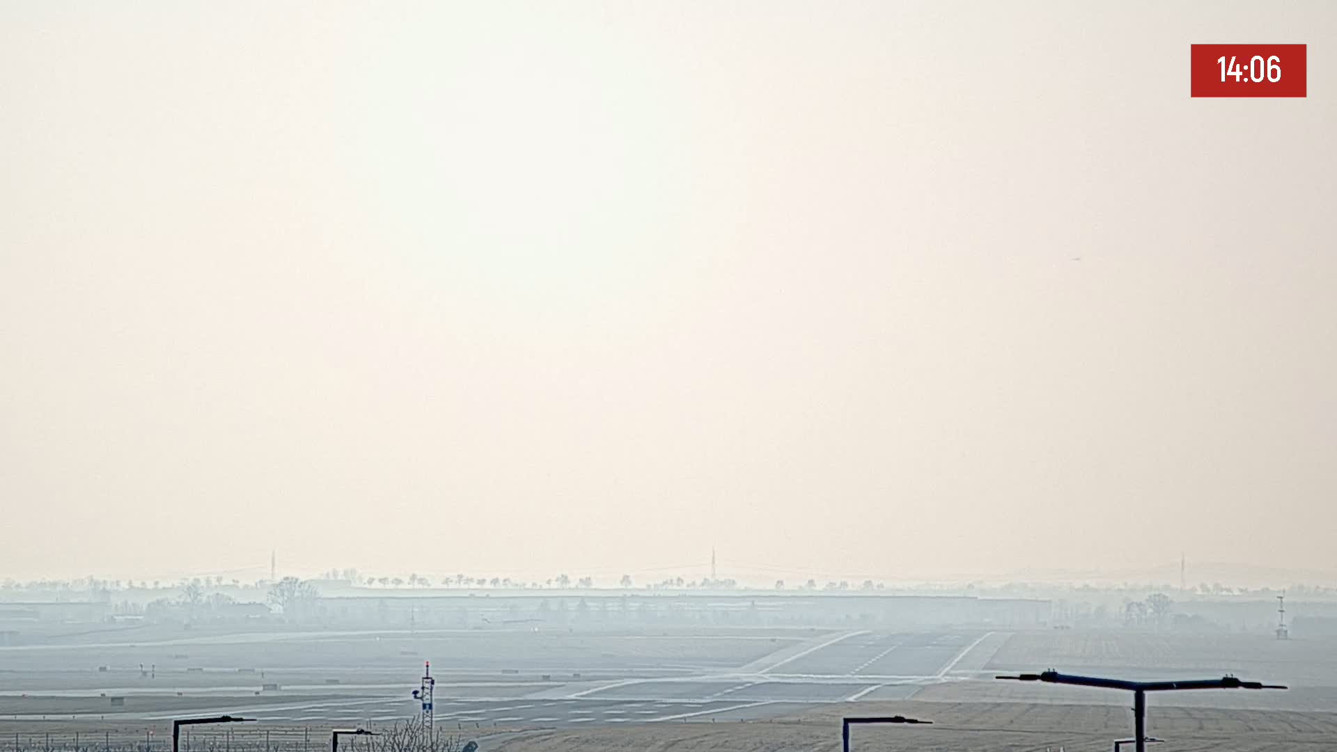 A hazy view of an airport runway and surrounding landscape under a bright, overcast sky.