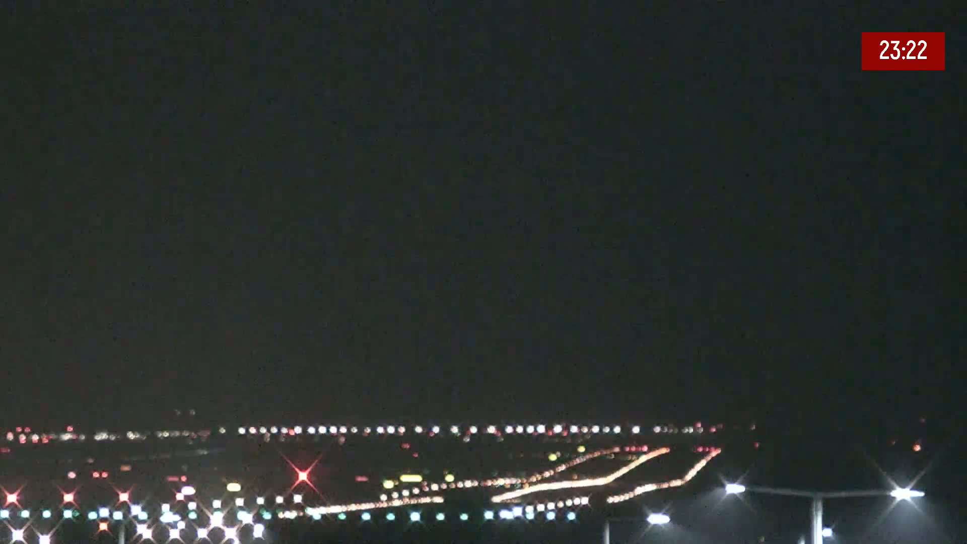 A nighttime view of a brightly lit airport runway and surrounding area under a clear, dark sky.