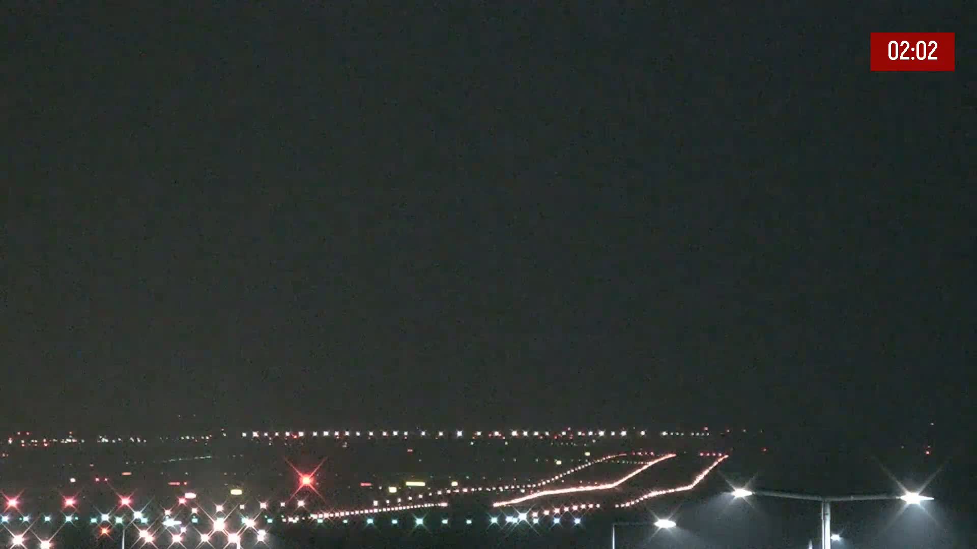 A nighttime long shot of an airport runway illuminated with lights under a dark sky.