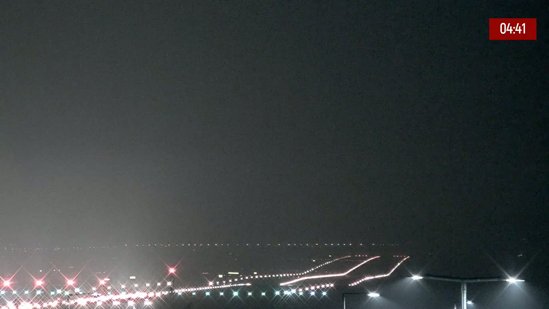 A long highway at night is dimly lit by streetlights under a hazy sky.