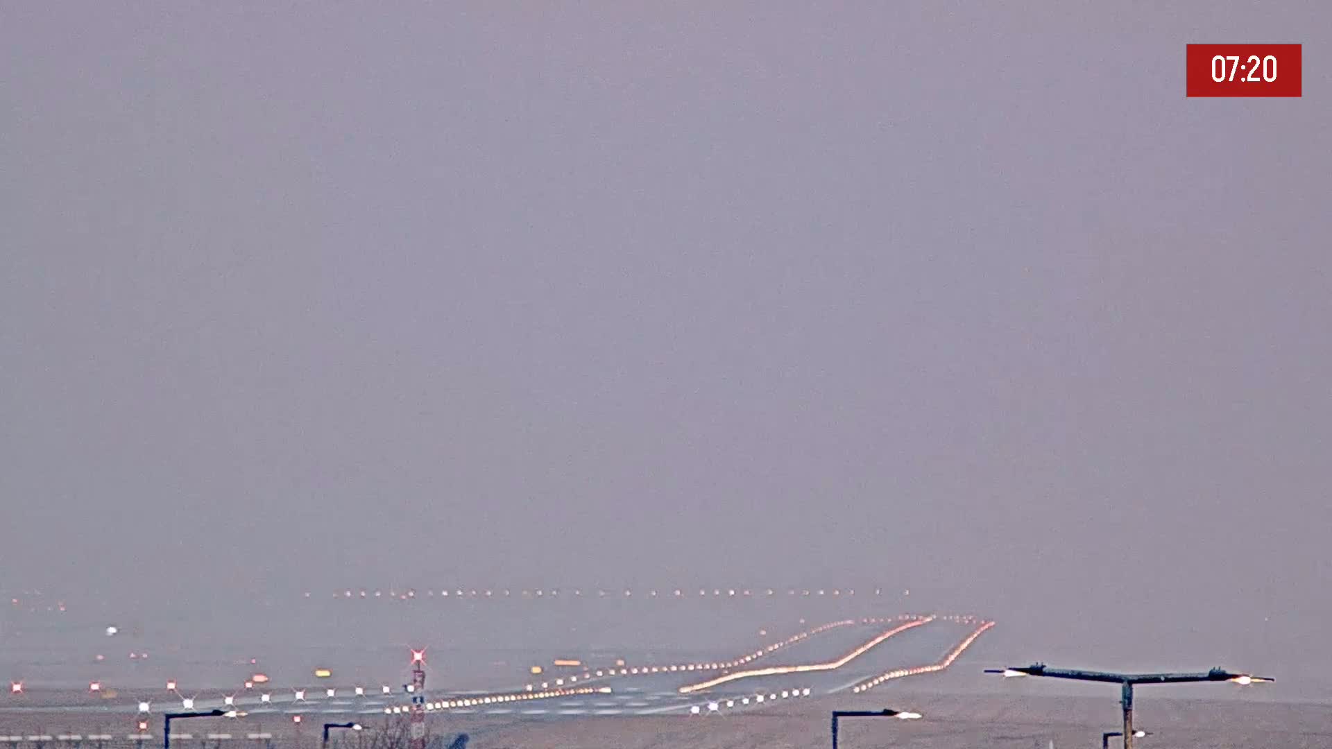 A hazy, low-visibility view of an airport runway with lights illuminating the landing strips.
