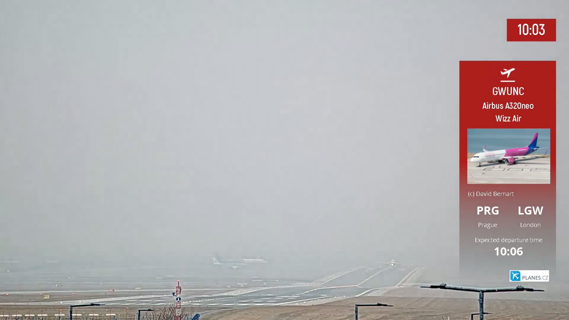 A foggy airport runway is shown with a distant airplane taxiing.