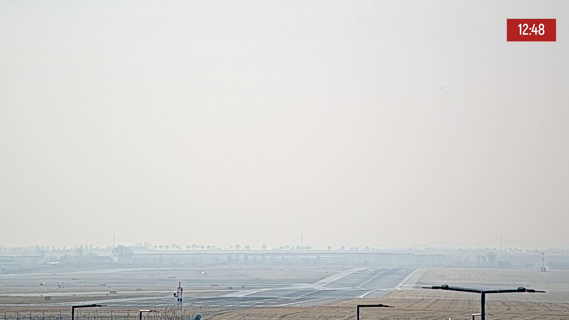 A hazy view of an airport runway and surrounding flat land is visible under a light, hazy sky.