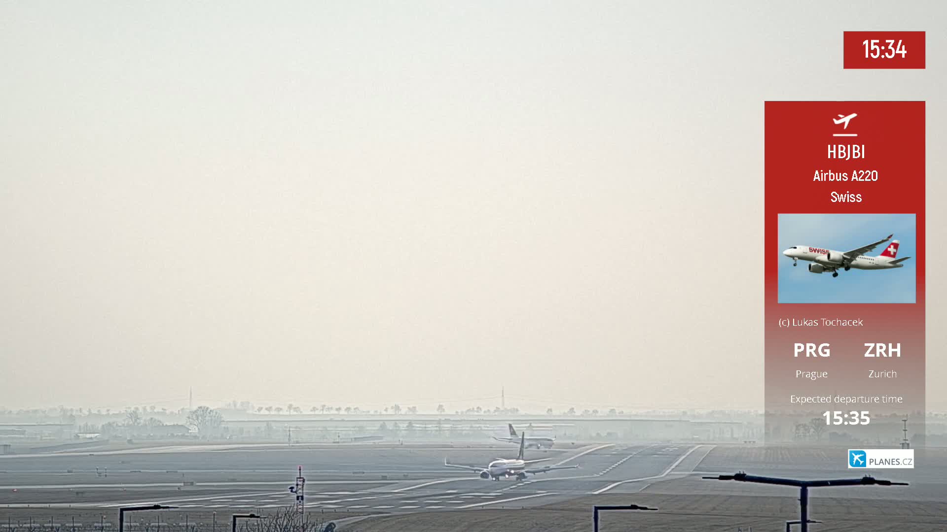 A hazy airport runway shows two airplanes, one taxiing and another taking off in the distance.