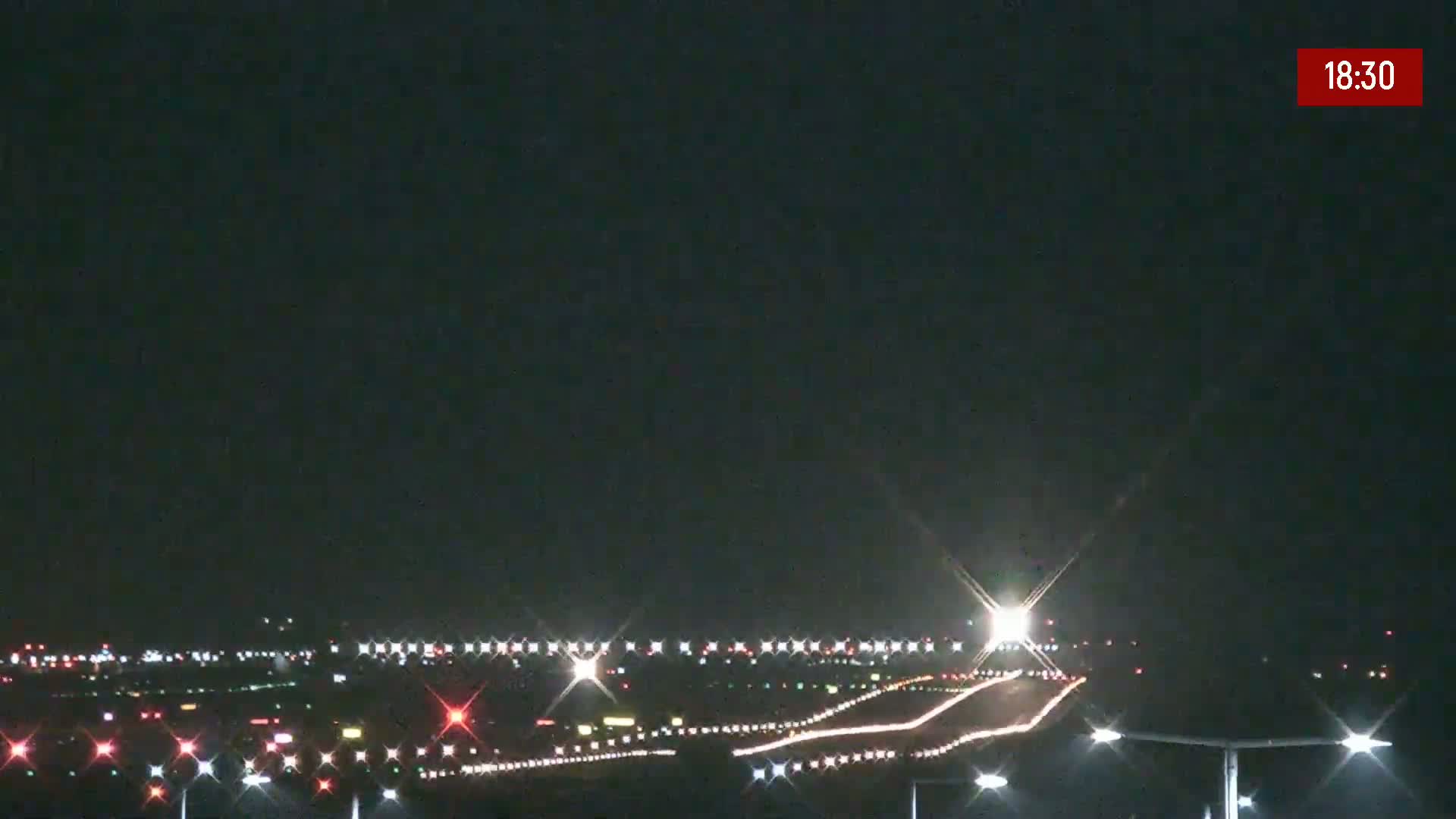 A nighttime view of an airport runway illuminated by bright lights under a clear, dark sky.