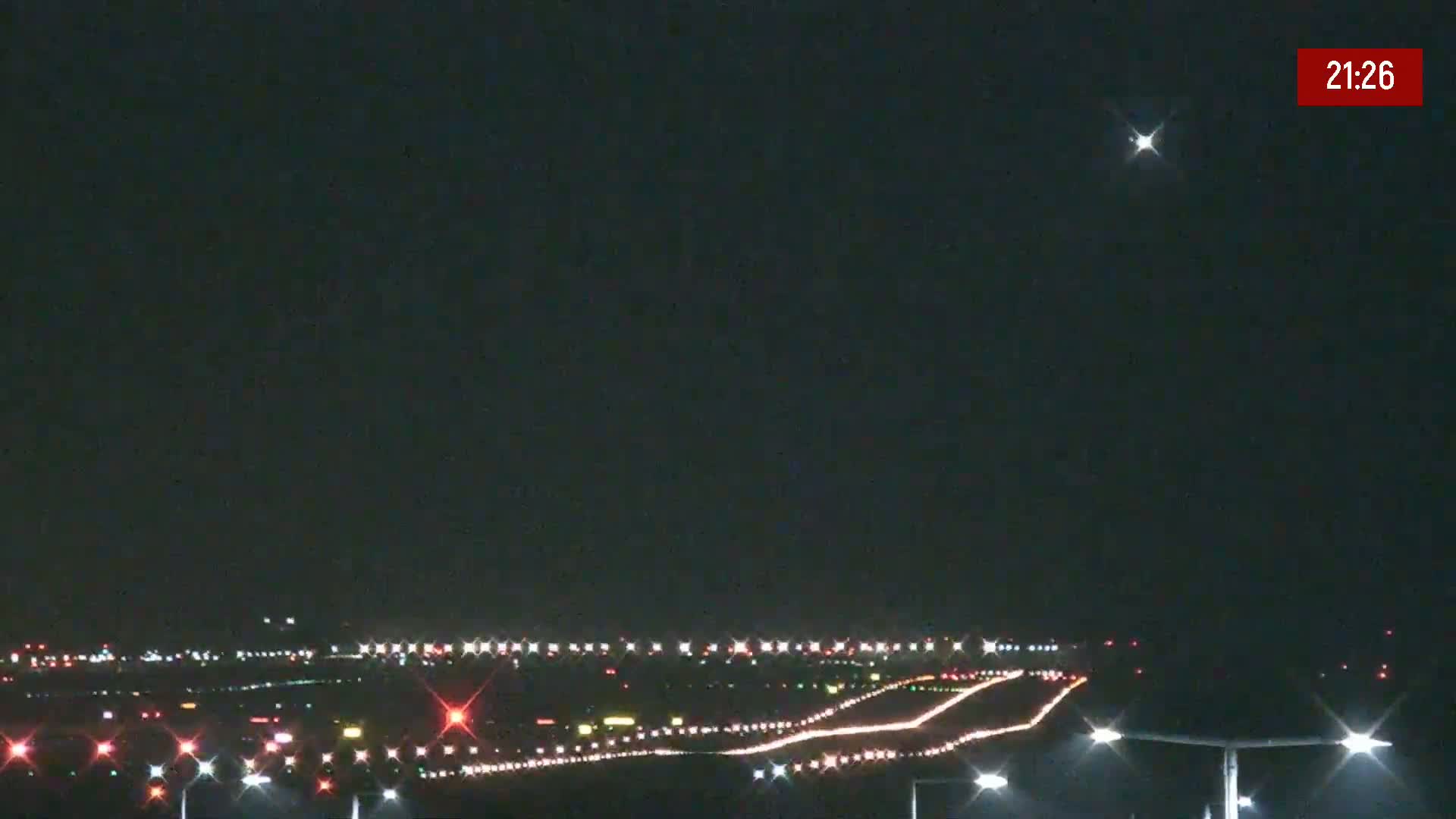 A nighttime view of an airport runway with lights illuminating the taxiways and the runway itself under a clear sky.
