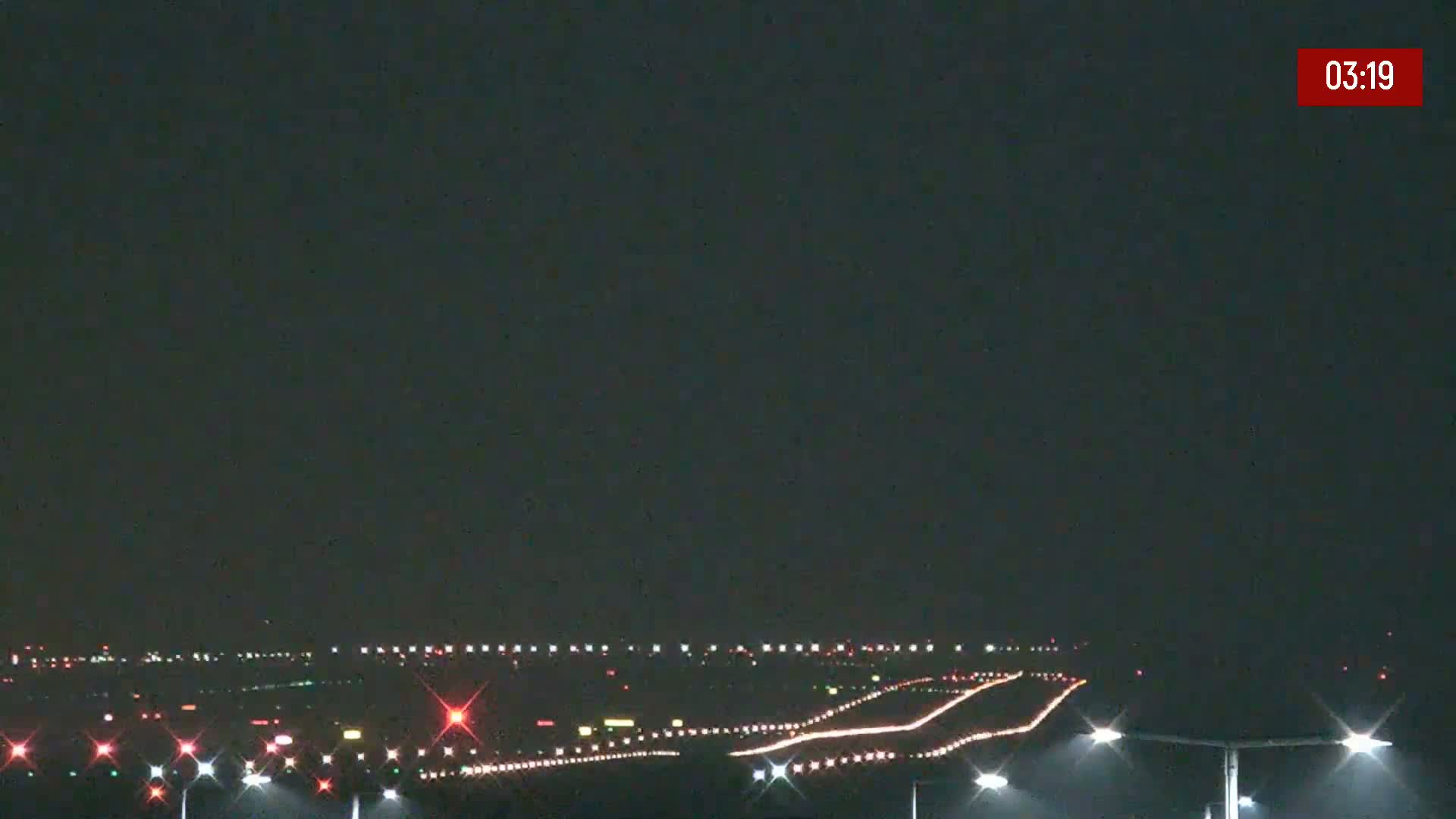 A nighttime view of an airport runway with lights illuminating the taxiways and runways under a dark sky.