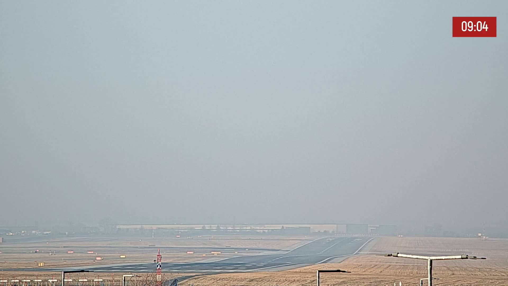 A hazy view of an airport runway and surrounding landscape on a foggy day.