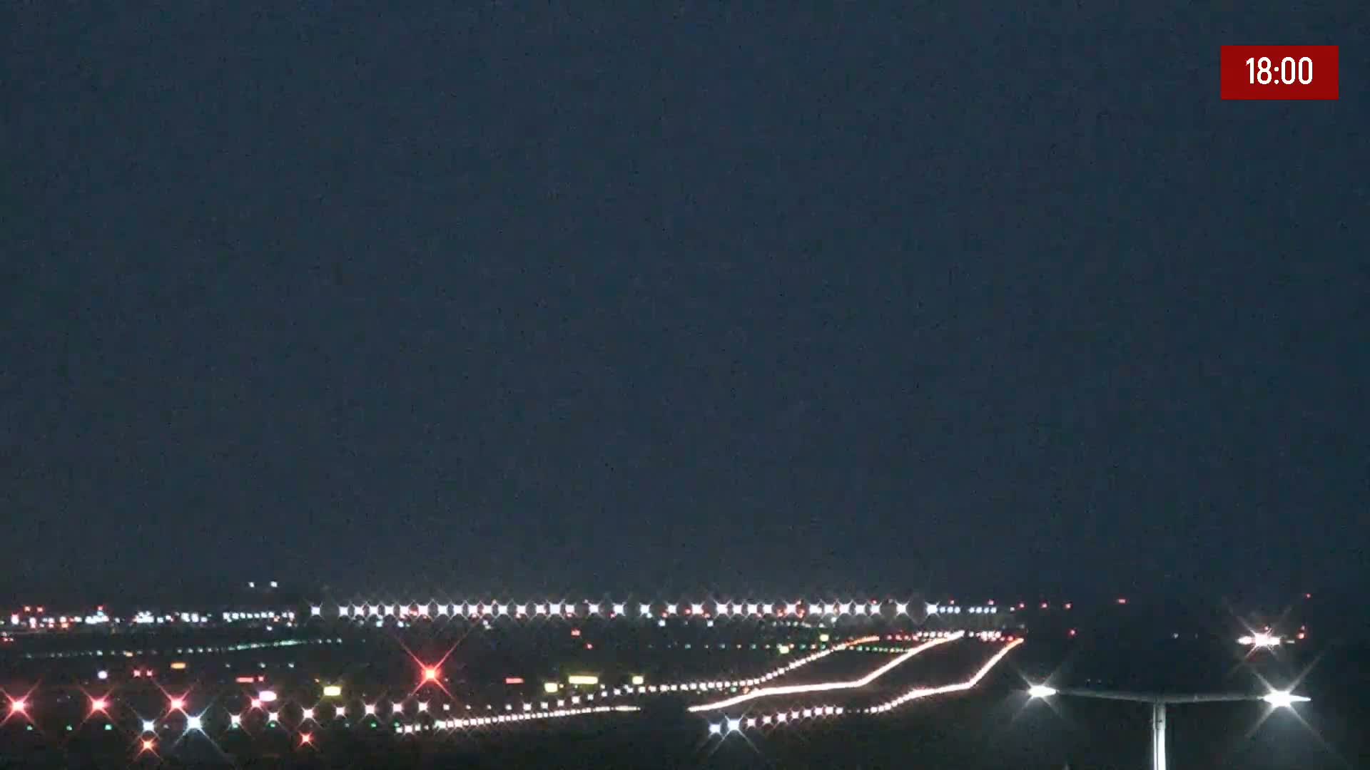 A nighttime view of an airport runway with lights illuminating the tarmac under a dark sky.