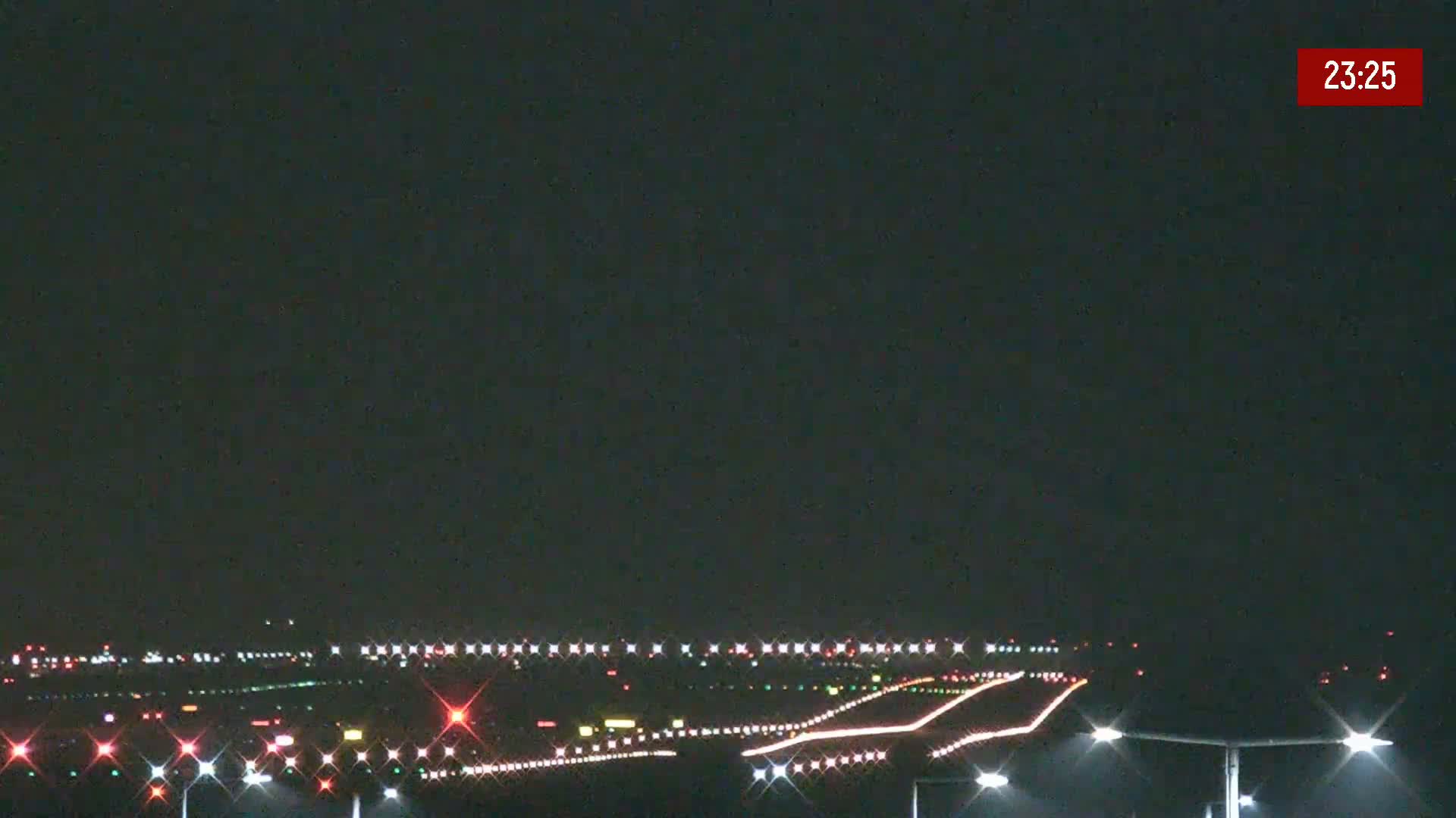 A nighttime view of an airport runway illuminated with lights under a dark sky.