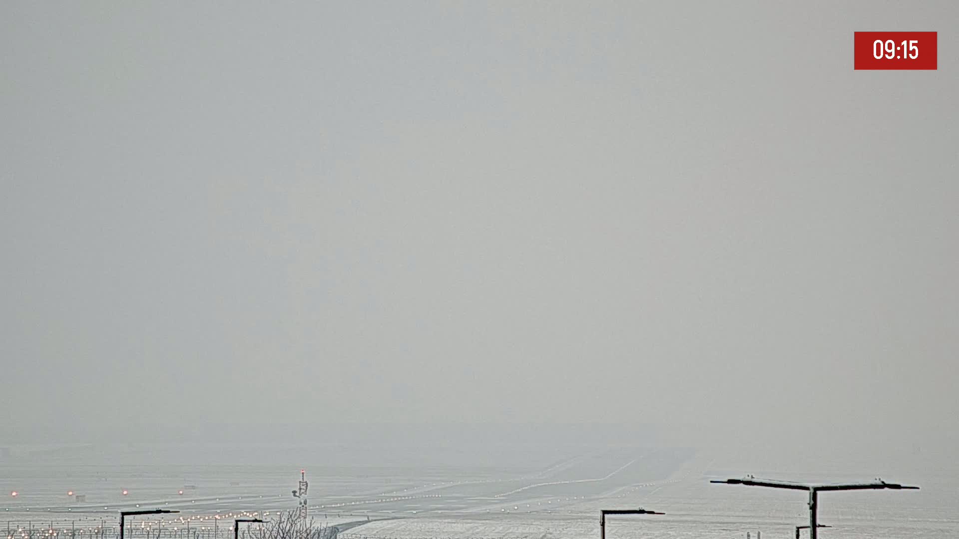 A snow-covered airport runway is barely visible through a thick fog.
