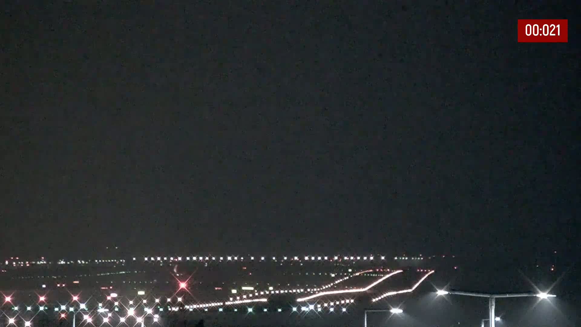 A nighttime view of an airport runway illuminated by lights under a dark sky.