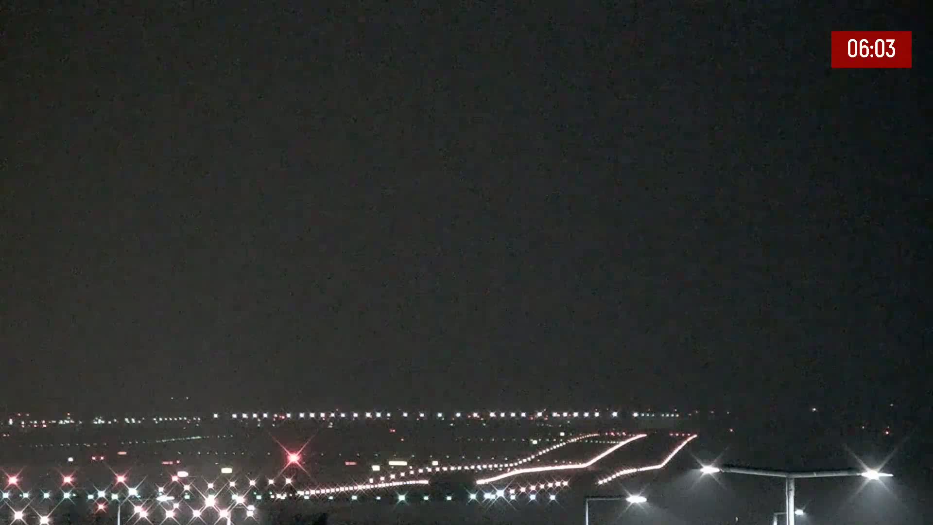 A nighttime view of an airport runway illuminated with lights under a dark sky.