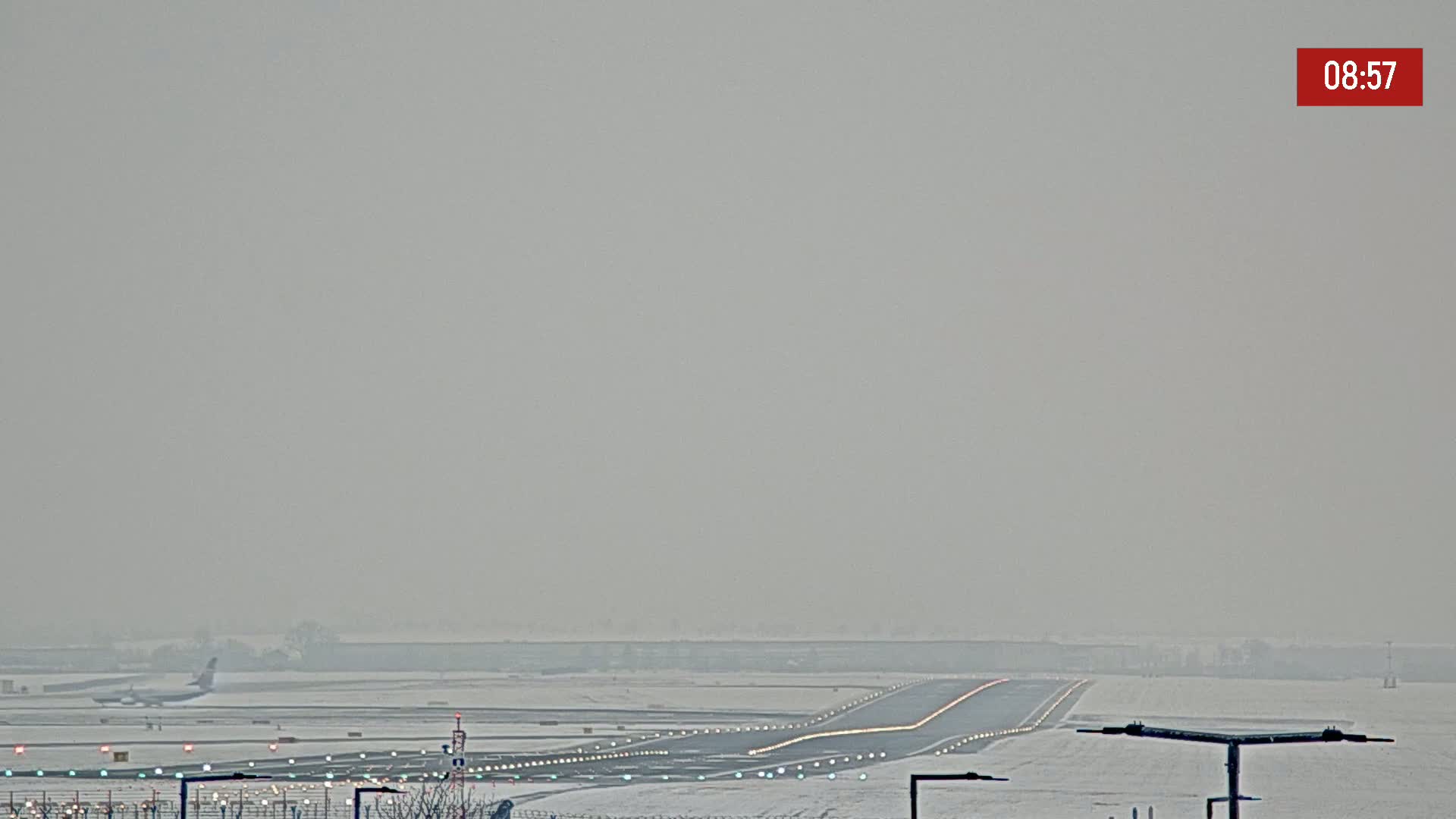 A runway covered in snow is visible, with an airplane in the distance on a hazy day.