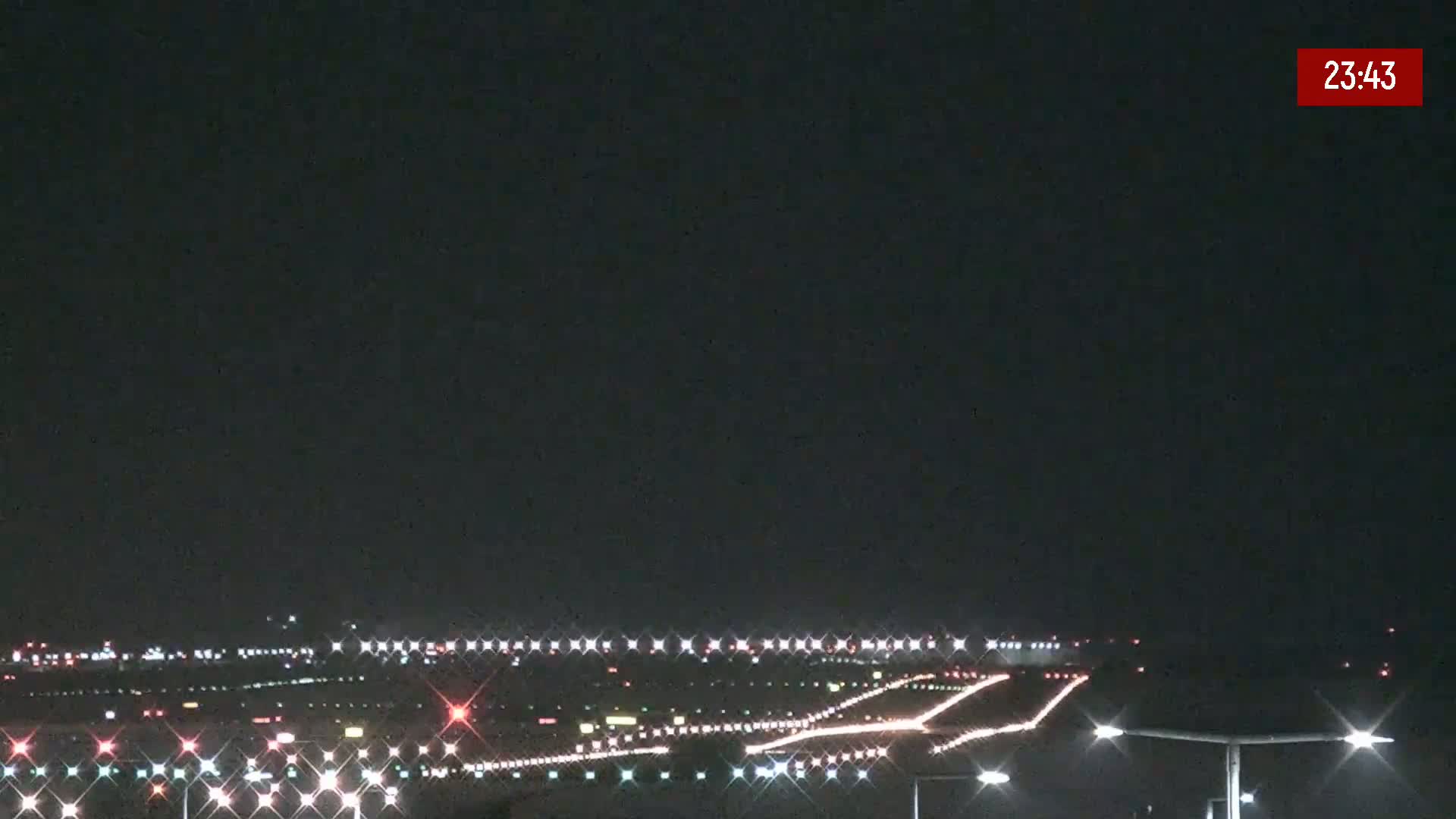 A nighttime view of an airport runway illuminated with lights under a clear, dark sky.